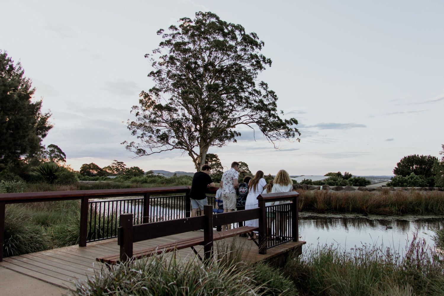 A panoramic view of a wooden boardwalk stretching along a serene lake with trees and people enjoying the scenery.