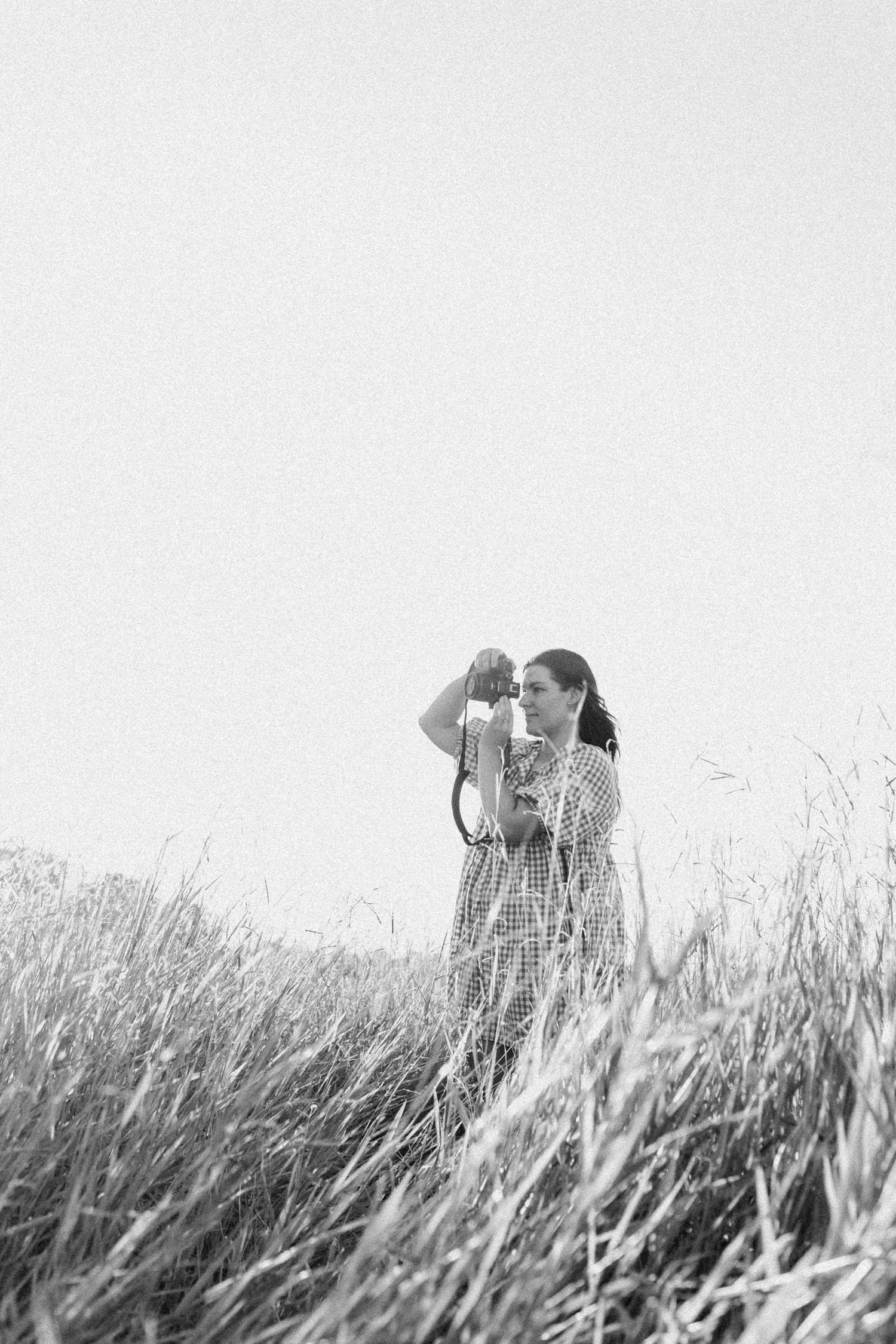 Black and white photo of a woman taking a photo in a field