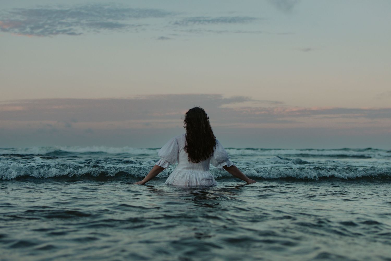 woman walking out into the water in a white dress