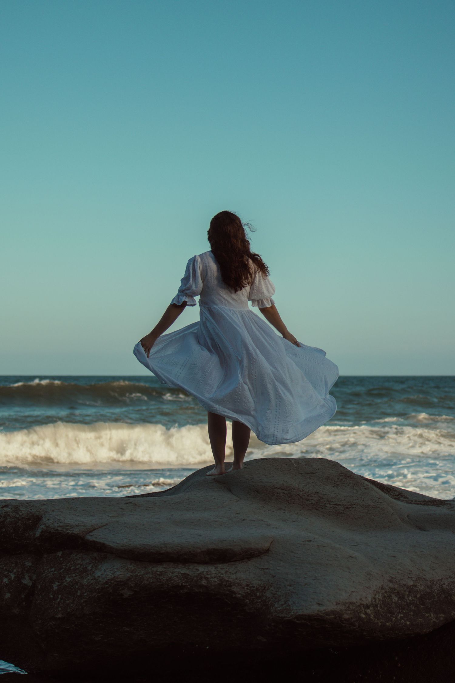 woman in white dress standing on a rock at the beach