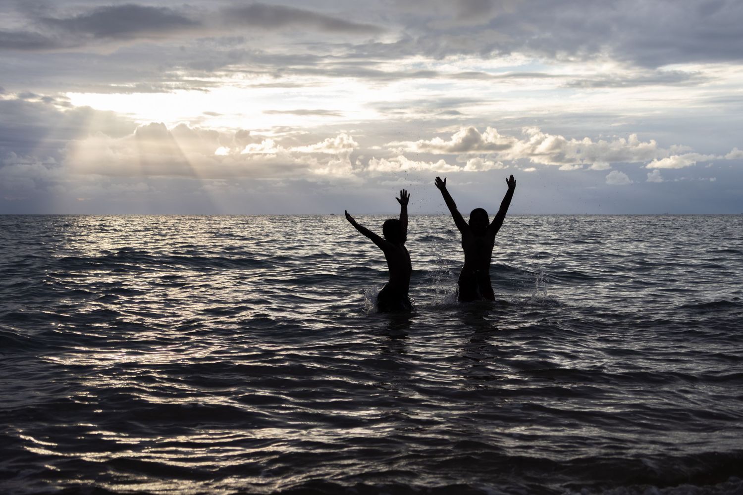 2 children jumping out of the water at sunrise