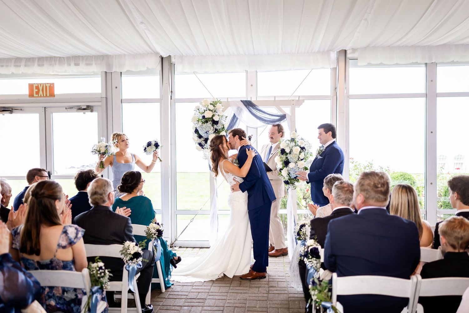Wedding reception setup in bright venue with blue and white table decorations and floral centerpieces.