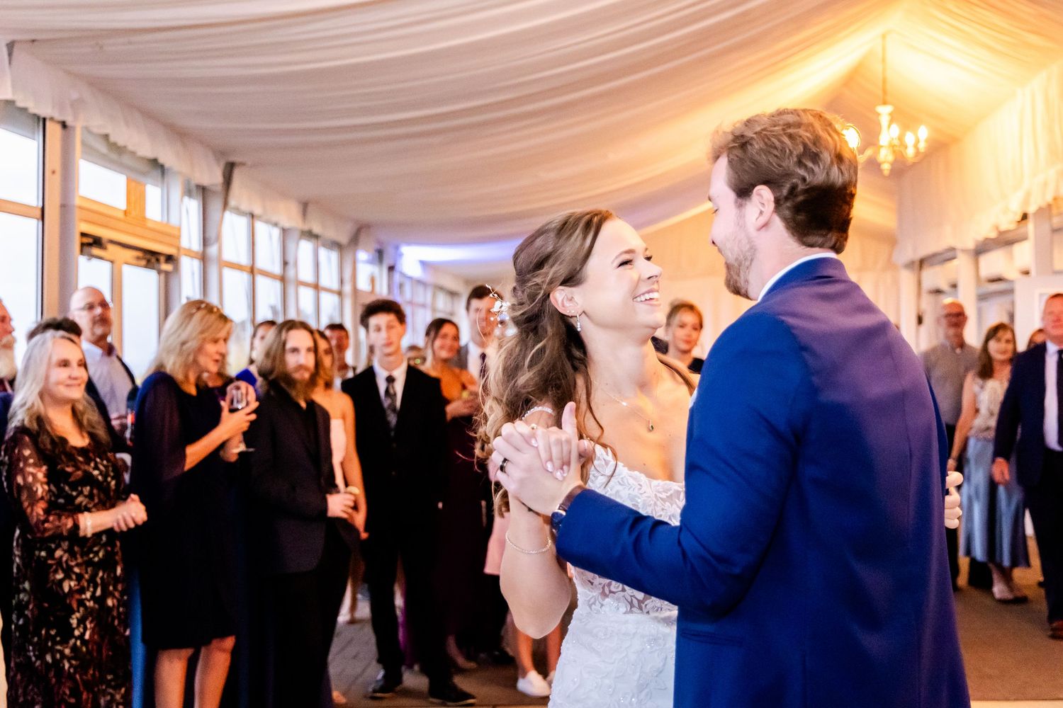 Wedding celebration in an elegant white-draped reception hall with chandeliers and ambient lighting.