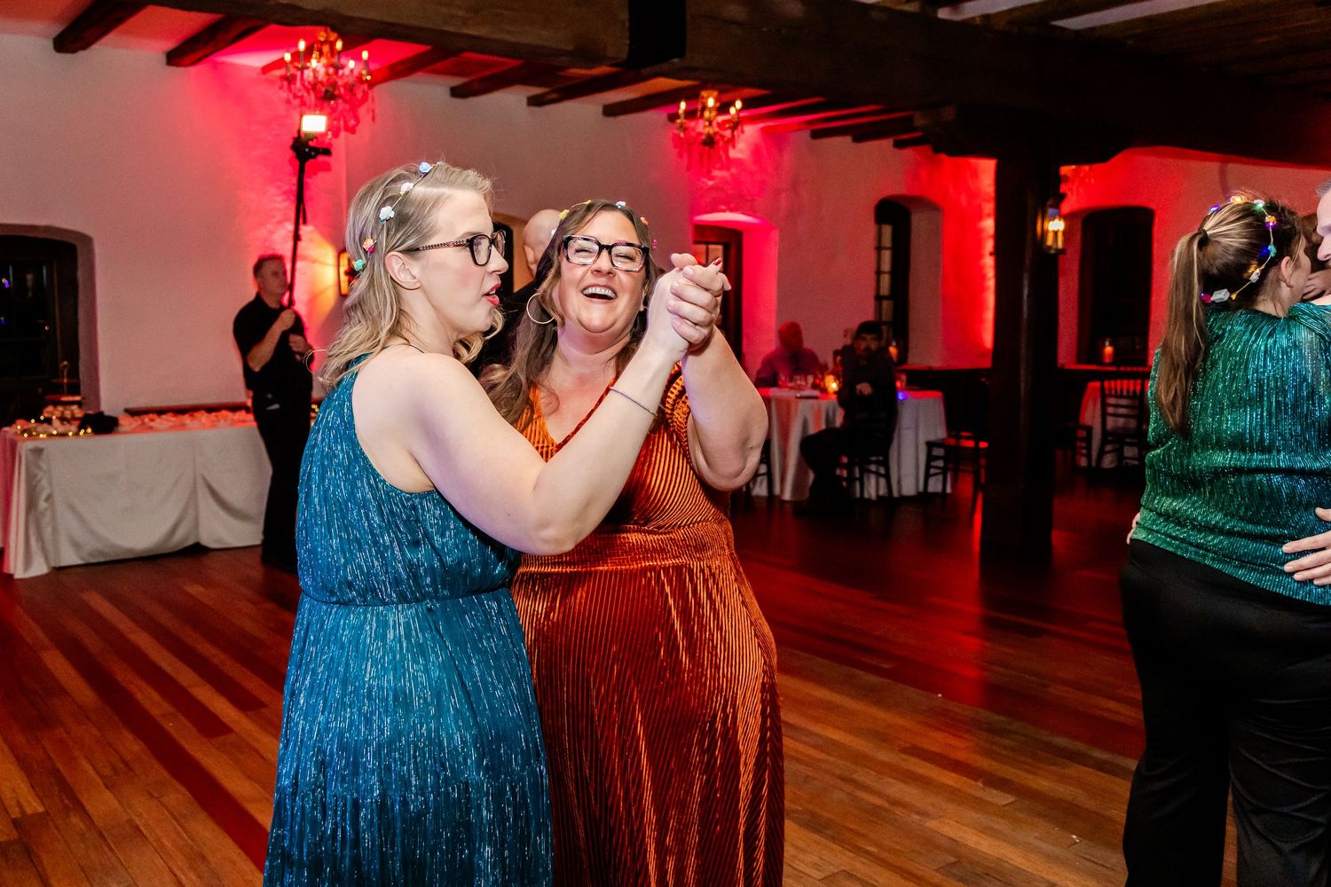 Wedding guests dancing together on wooden floor under red lighting.