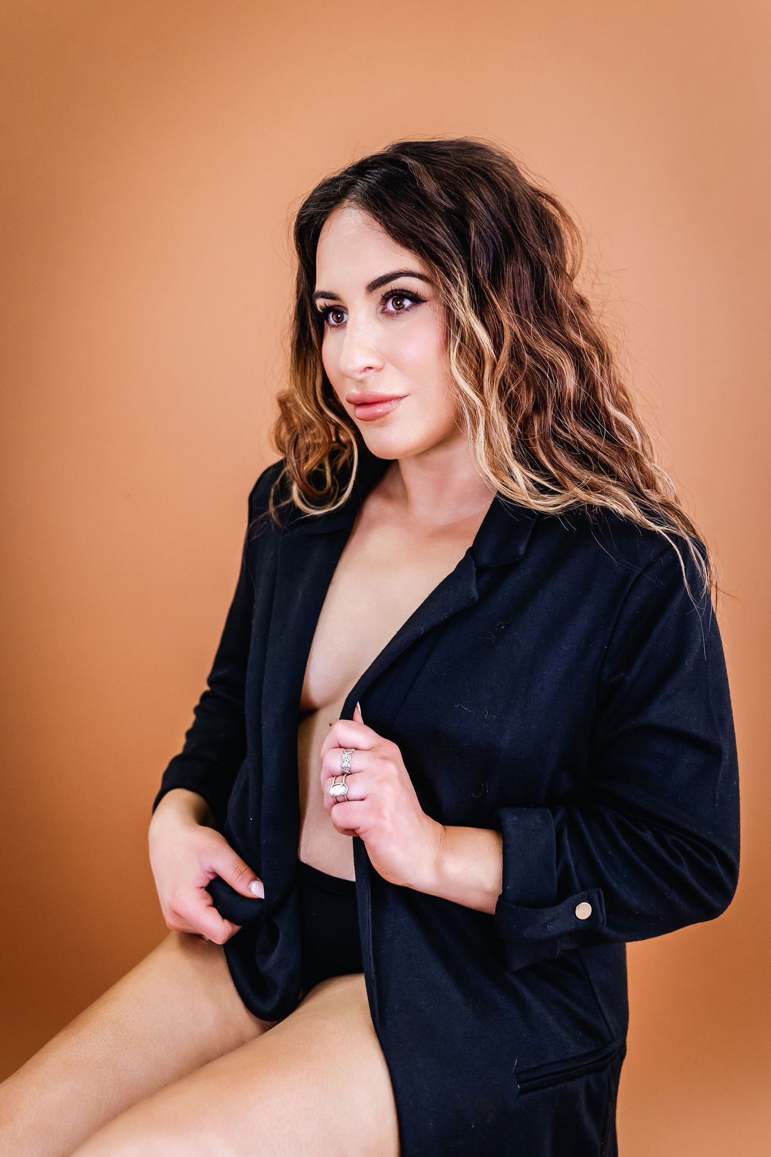 Portrait of someone in a black blazer with wavy highlighted hair against an orange background.