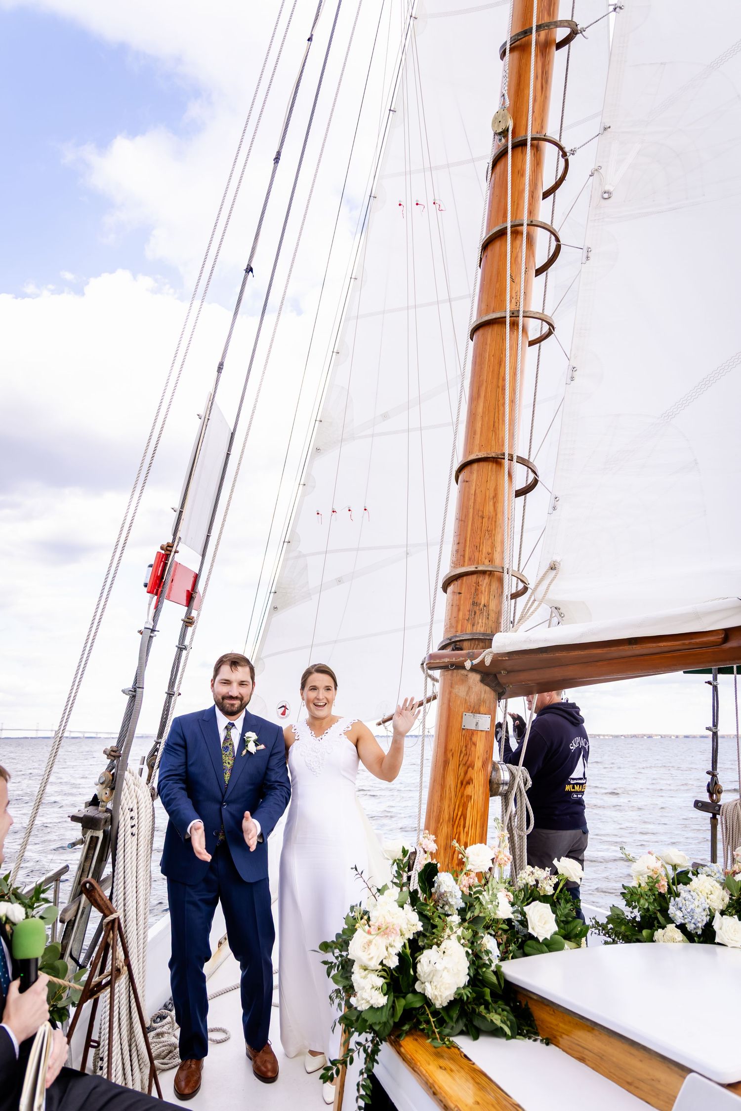 Bride and groom standing on sailboat deck with white floral arrangements during wedding ceremony.