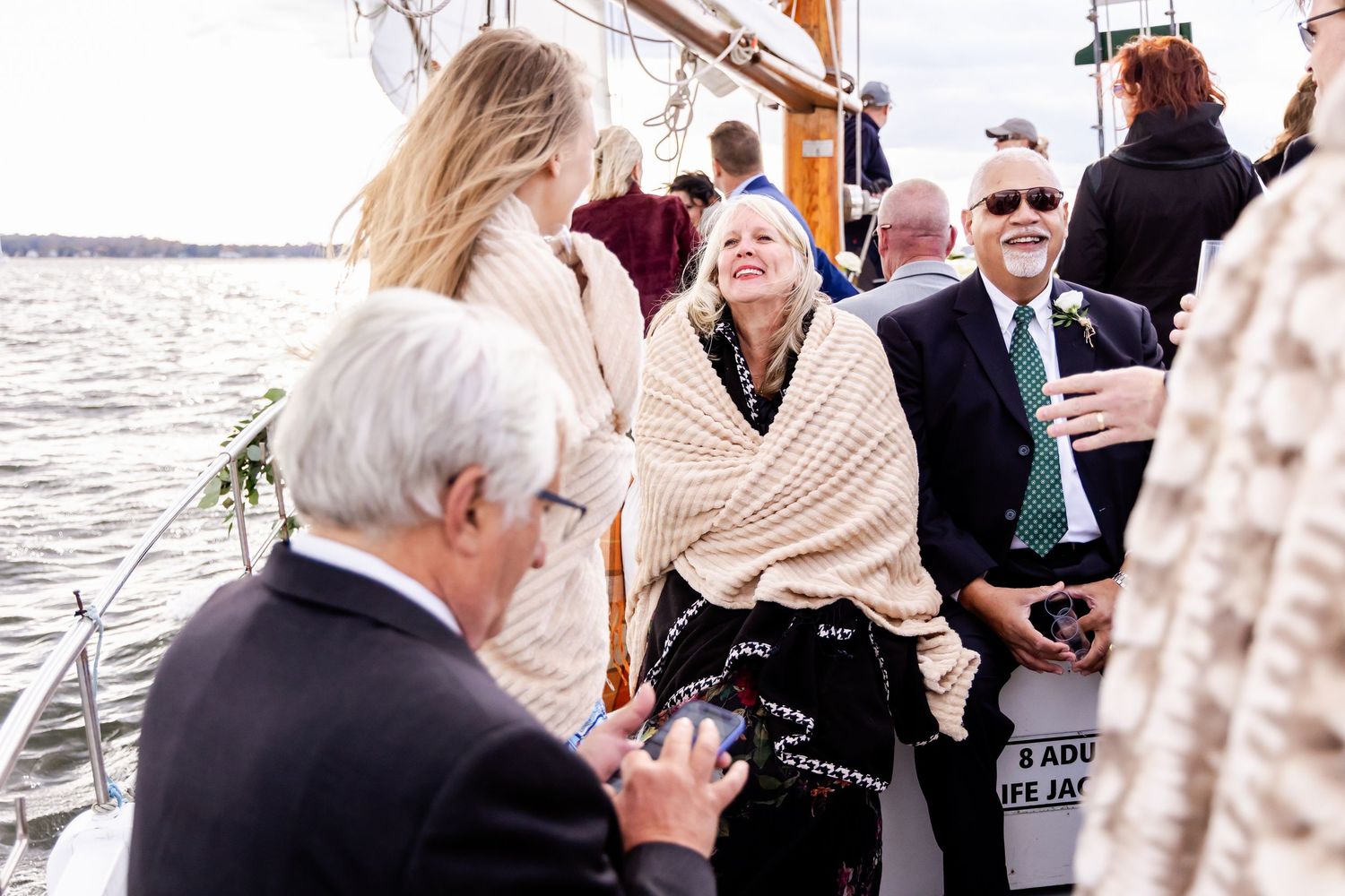 Guests socializing on a sailboat deck during an outdoor wedding celebration on the water.