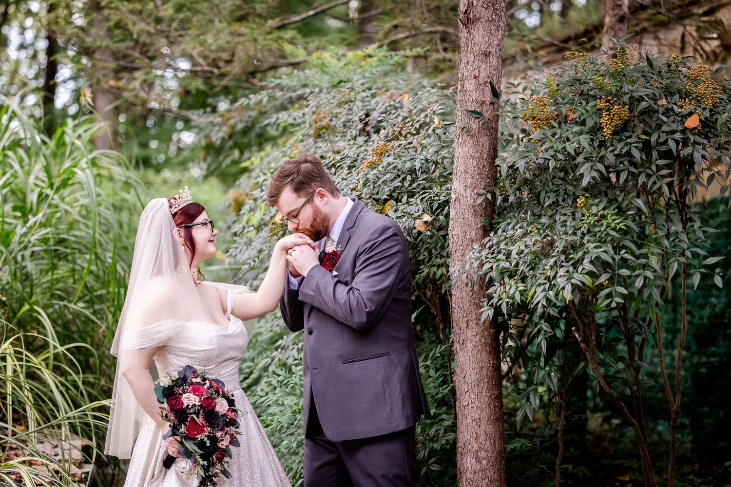 A romantic couple in wedding attire shares intimate moments together in a lush forest setting with tall pine trees.