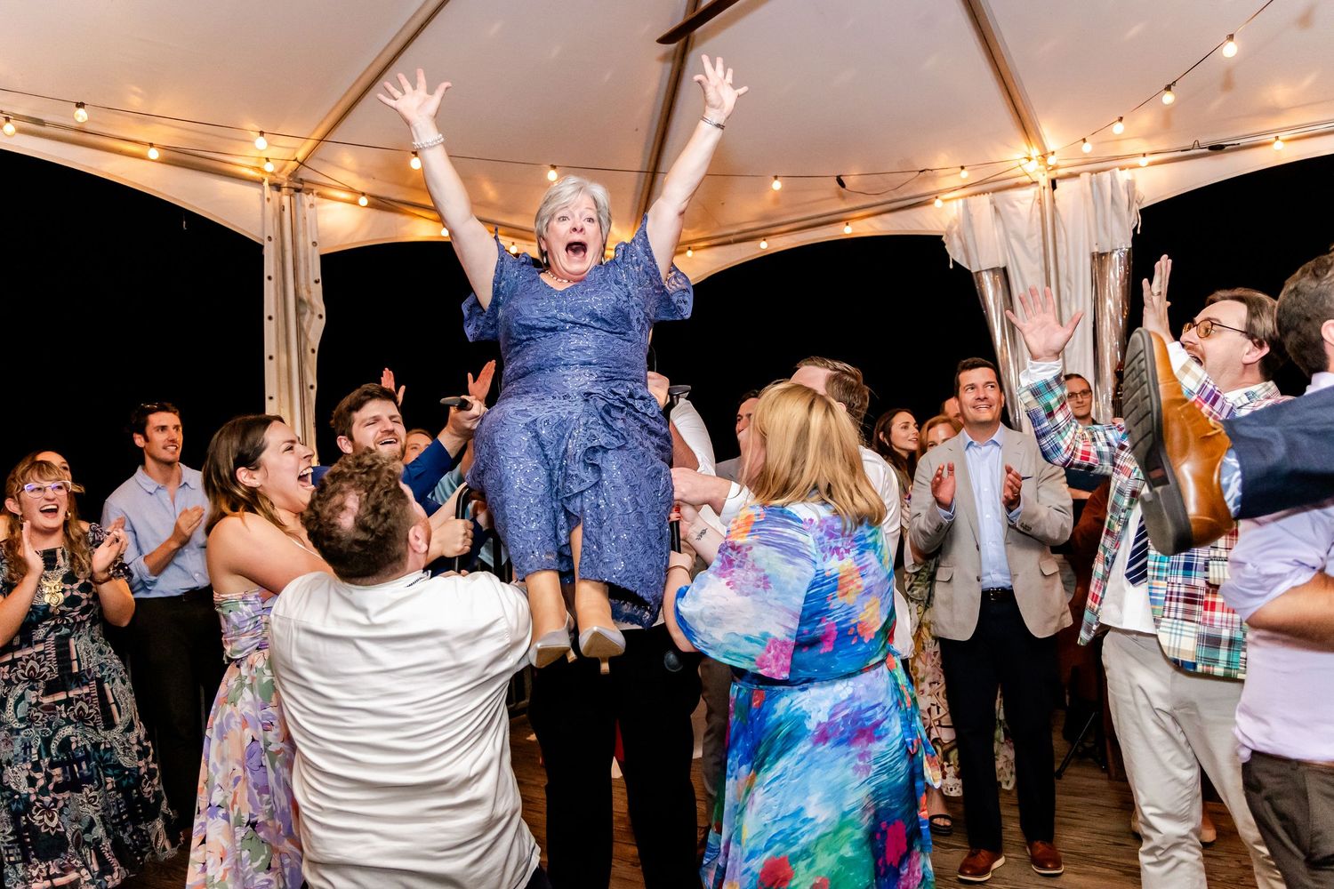 Energetic party scene at a wedding reception under a tent with people dancing and celebrating on the dance floor.