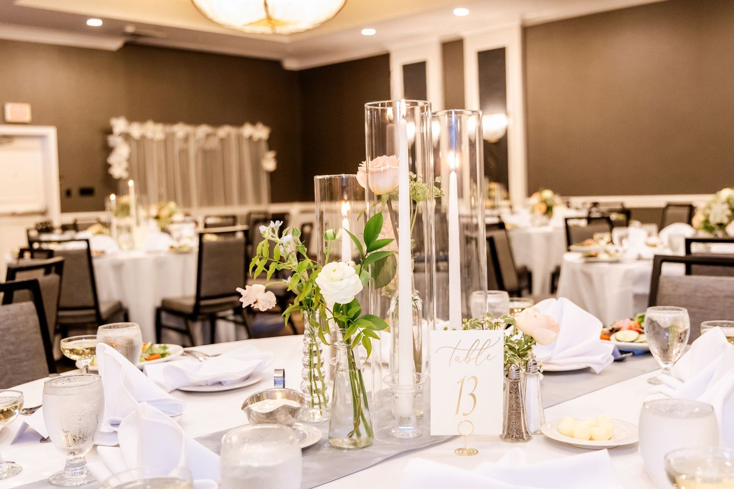 Elegant wedding reception tables decorated with white linens, floral centerpieces and ambient lighting in a banquet hall.