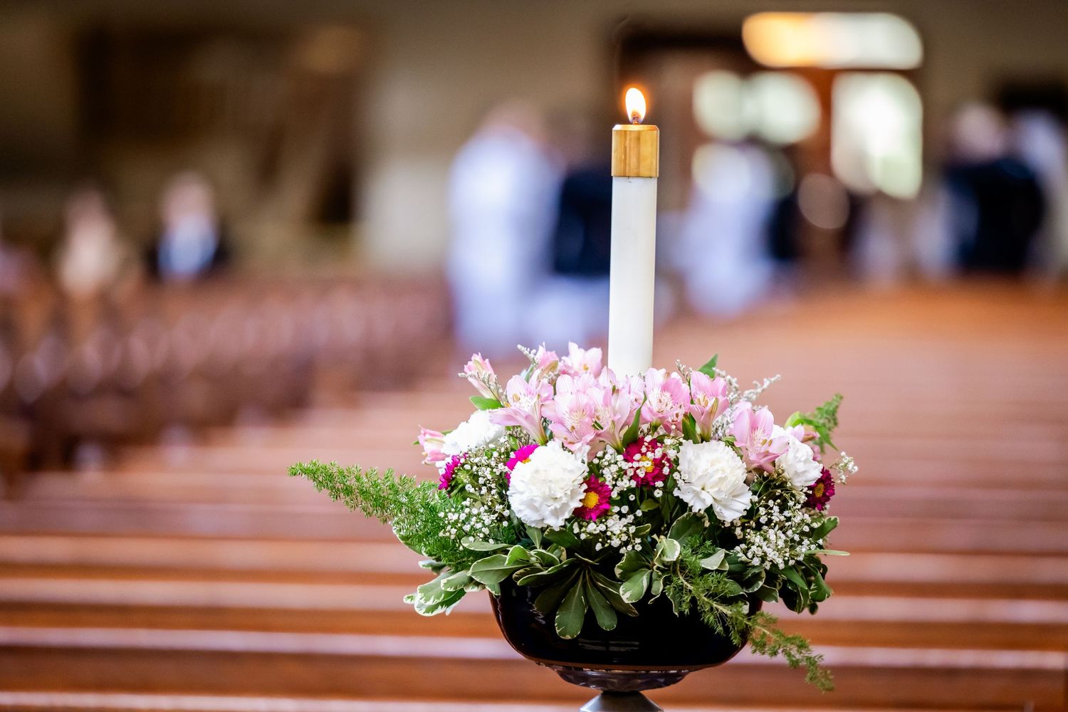 Church pews decorated with floral arrangements and candles for a wedding ceremony.