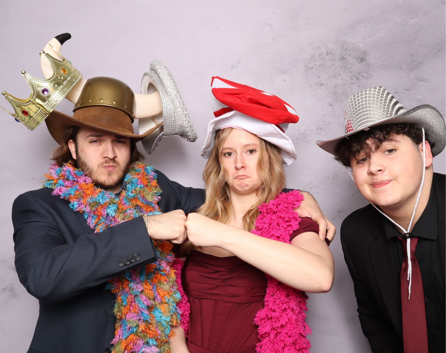 Three people in festive party attire with hats and accessories pose together at a photo booth.