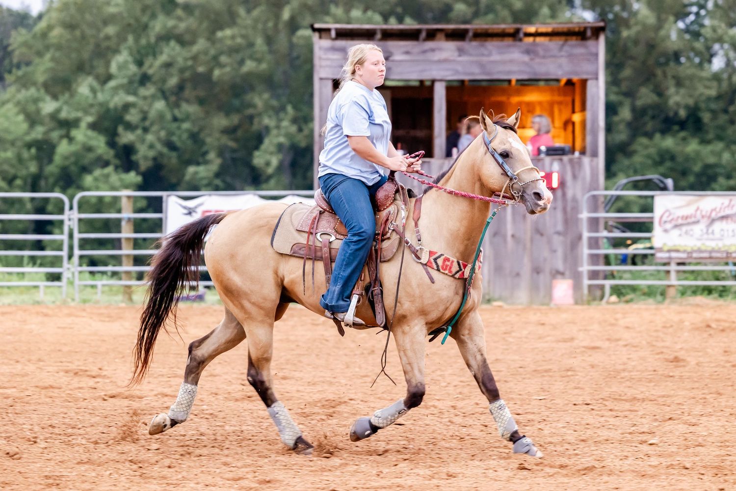 Horse and rider galloping through arena during western riding competition.