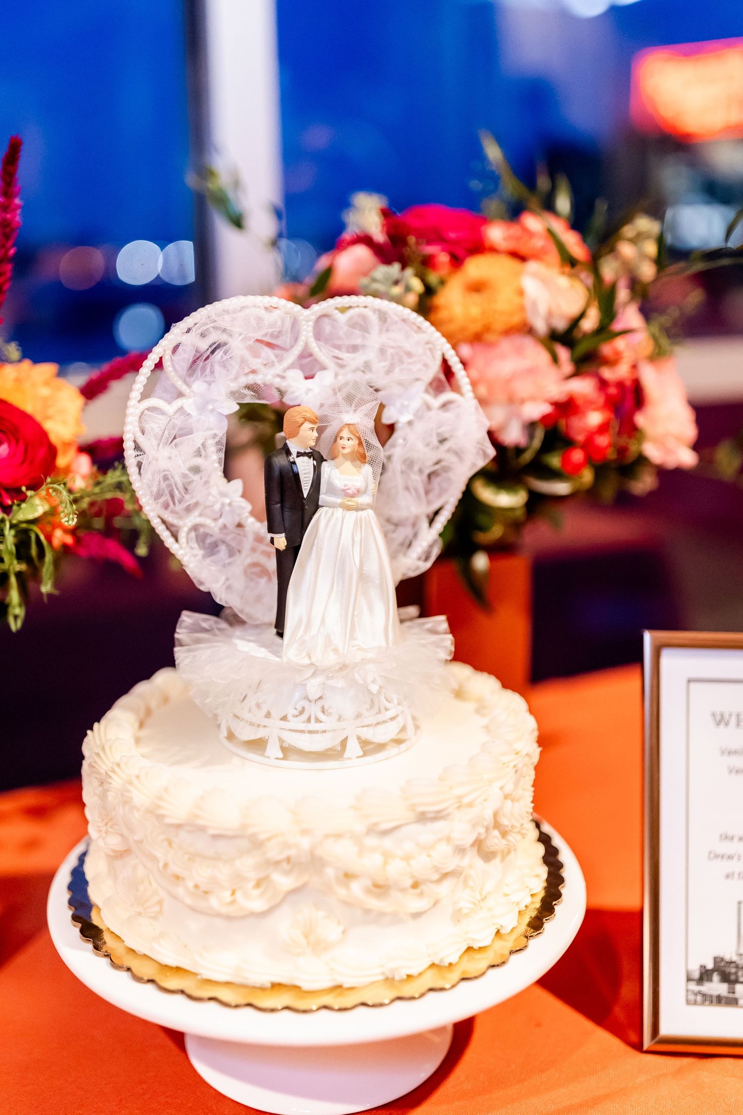 Wedding cake topped with crystal heart and bride groom figurines surrounded by floral decorations.