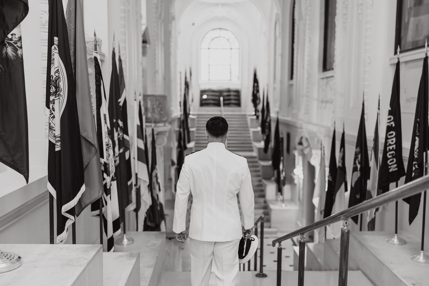 A black and white photo shows someone walking down a hallway lined with military flags and banners.