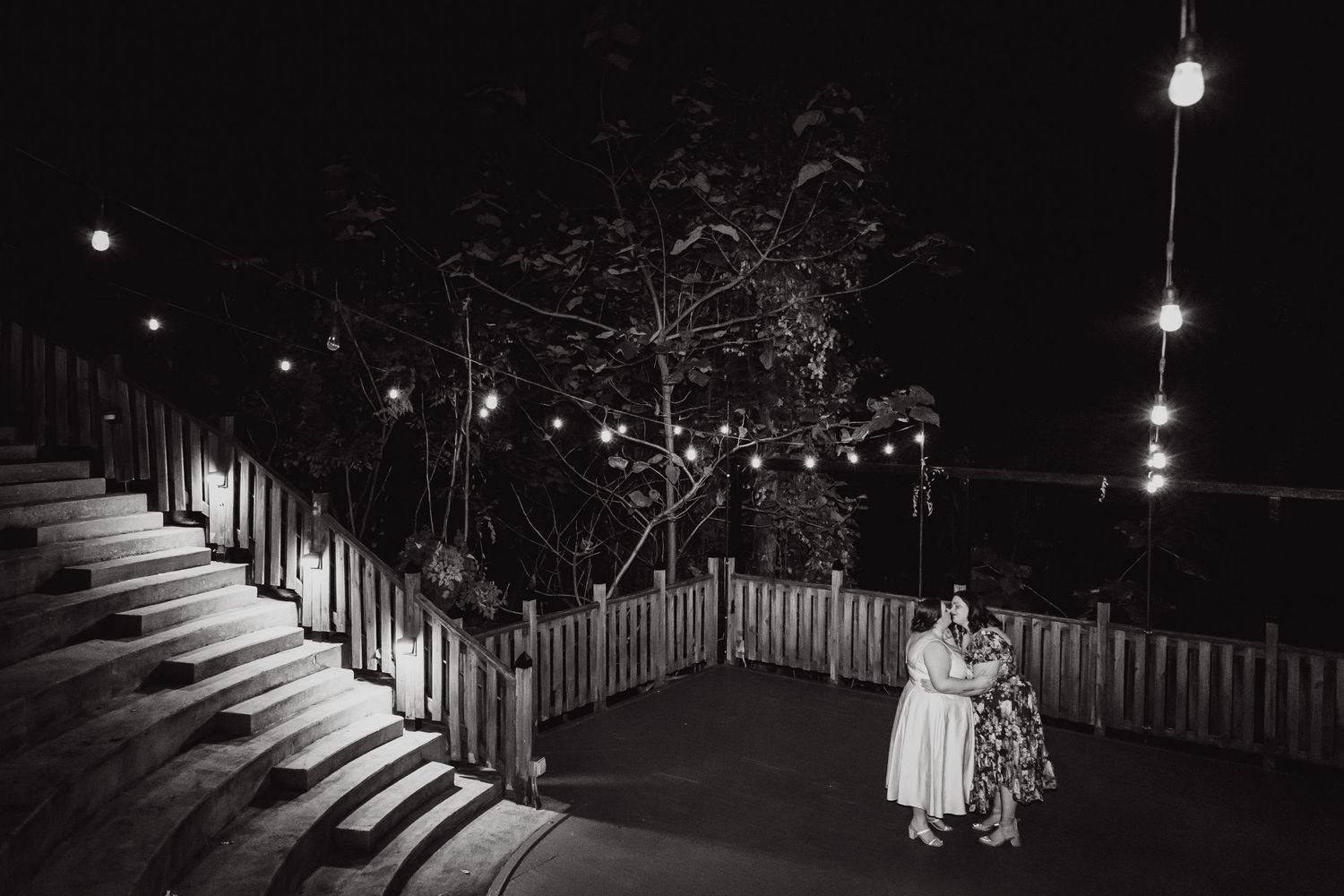 Black and white nighttime wedding photo with string lights illuminating outdoor deck stairs.