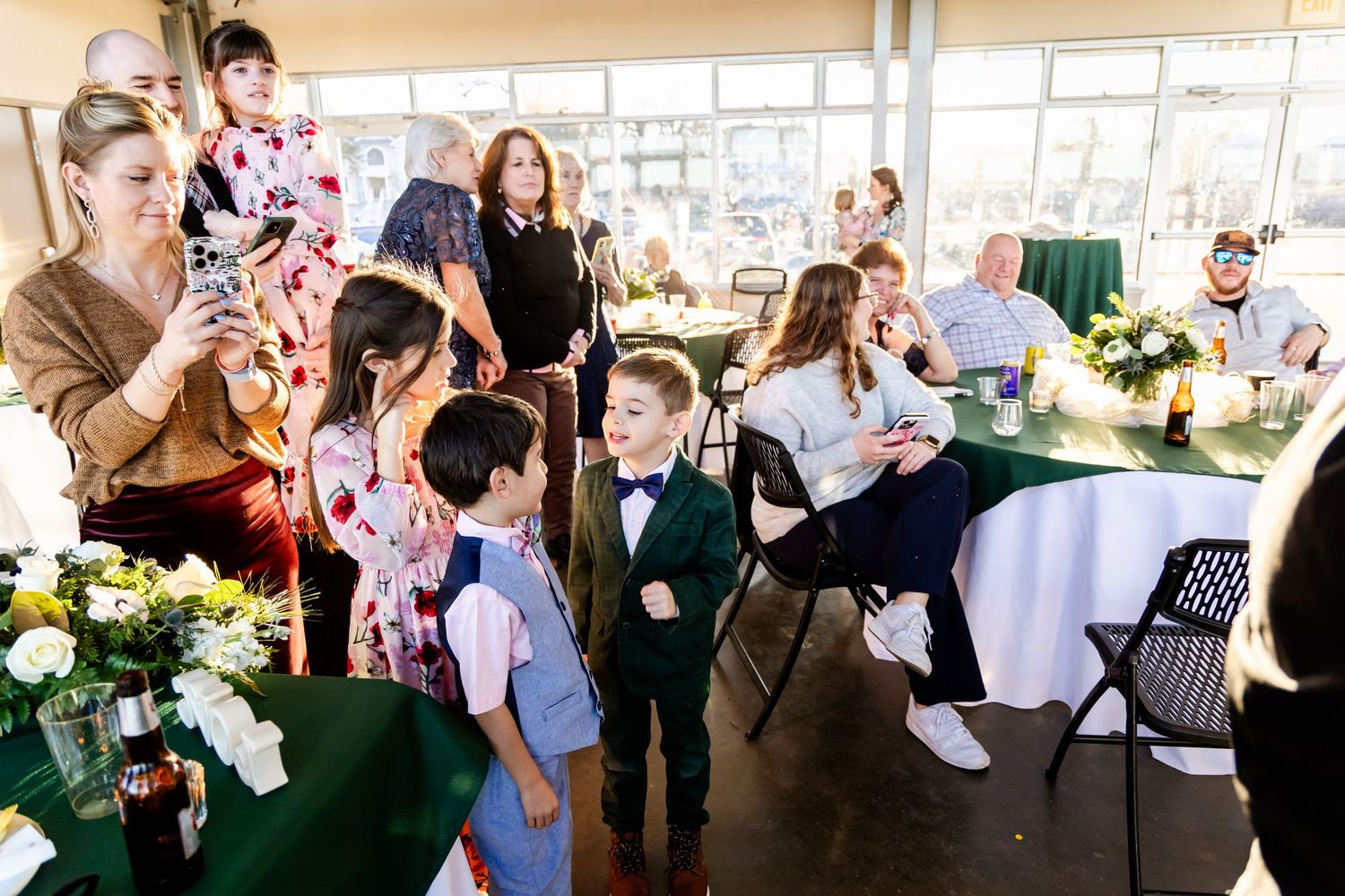 Wedding guests gather inside an elegant reception tent with white floral centerpieces and round tables.