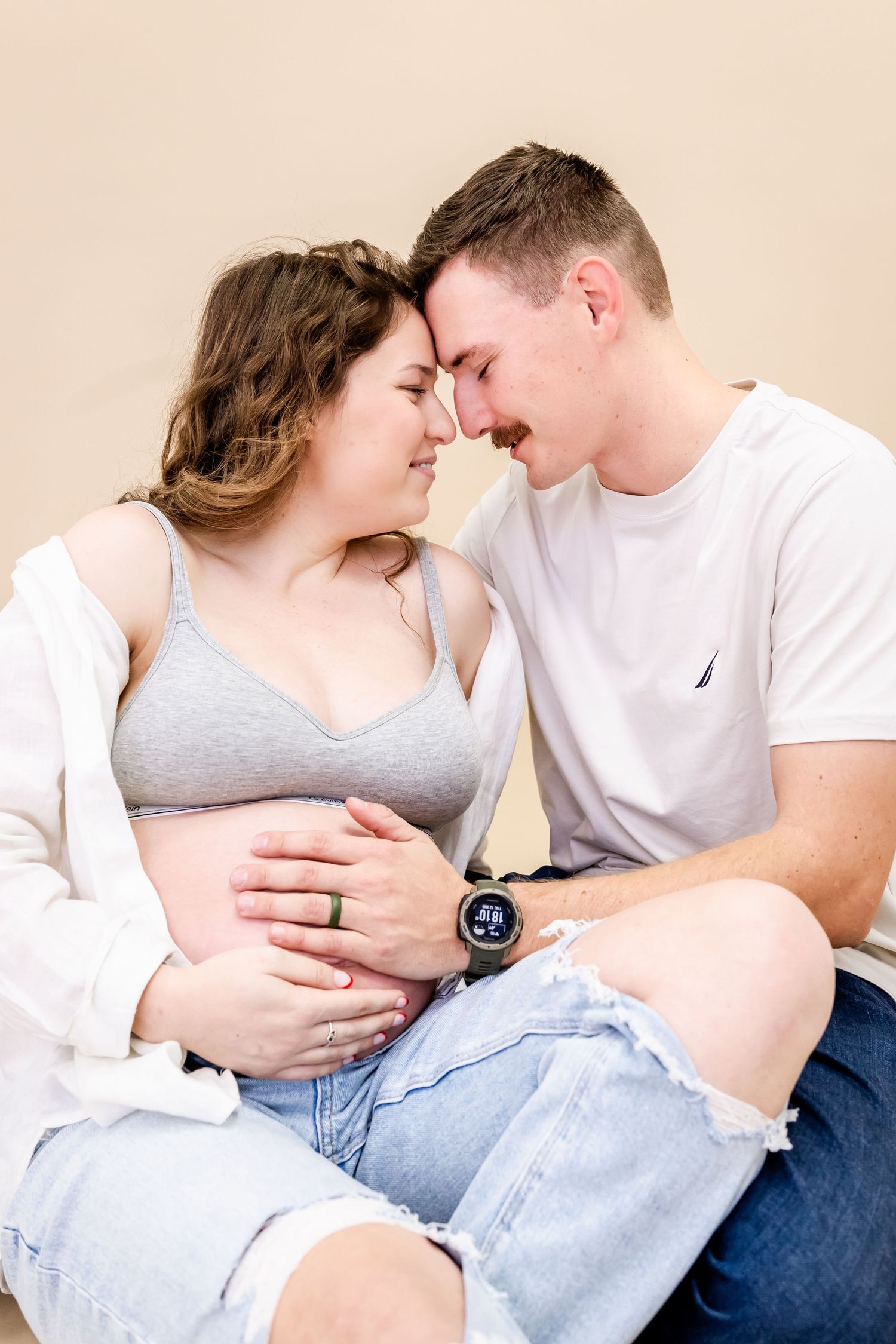 Intimate maternity photo of expecting couple touching foreheads while hands rest on pregnant belly.