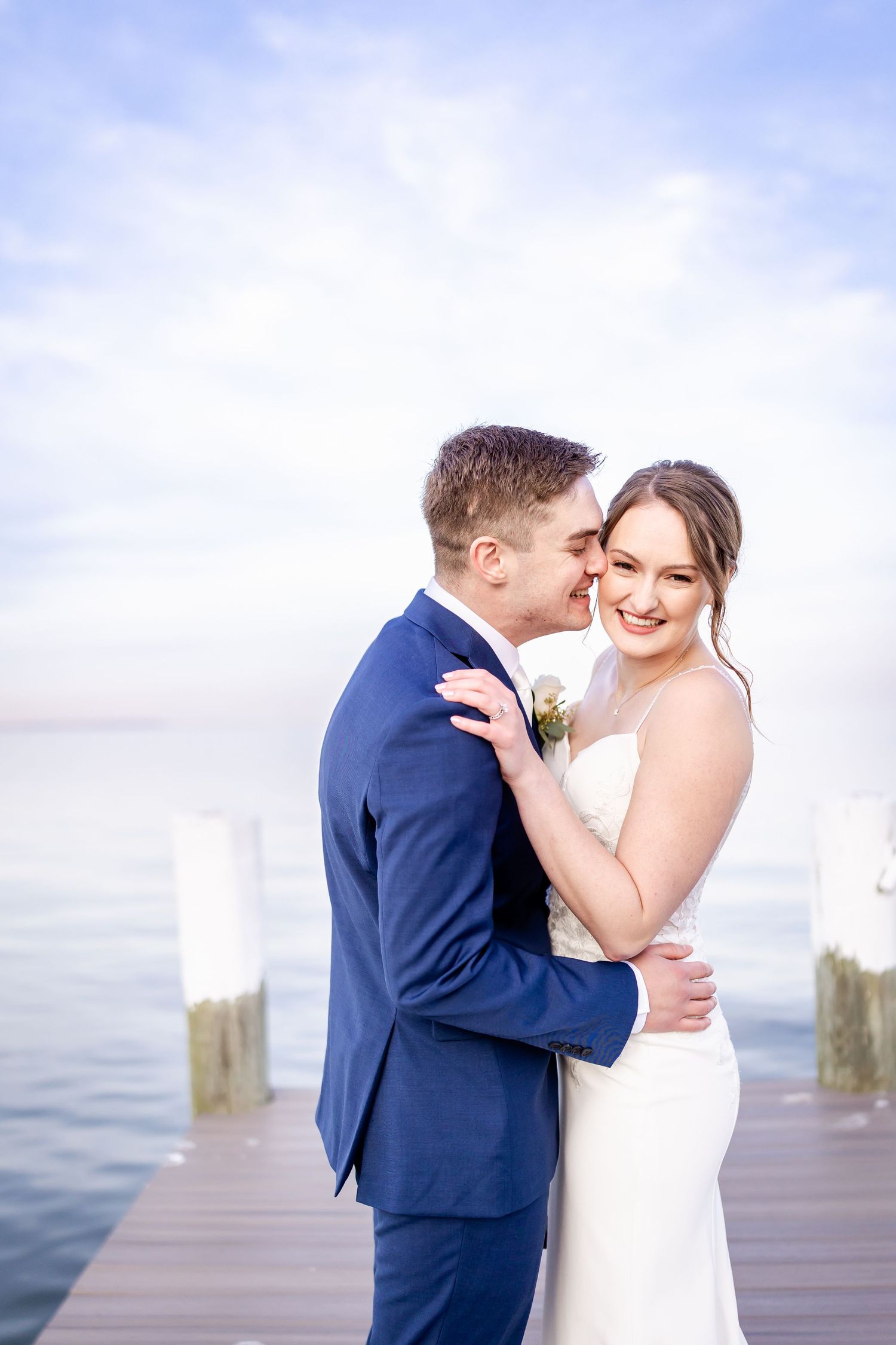 Romantic couple shares intimate moments on a wooden dock by the water during their wedding.