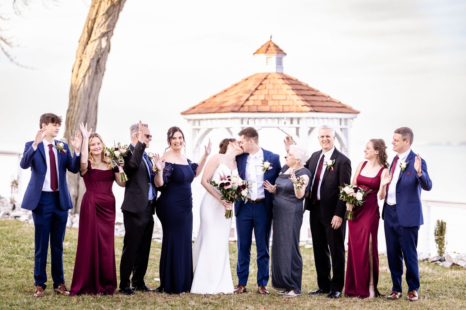 Large wedding party stands in line on boardwalk with gazebo in background.