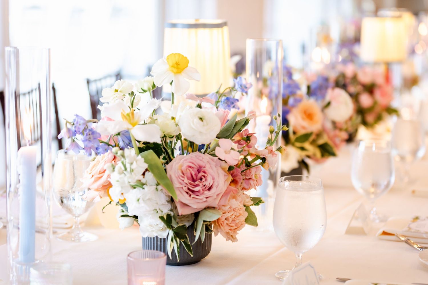 Elegant floral centerpiece with pink roses and mixed flowers in glass vase on wedding reception table.