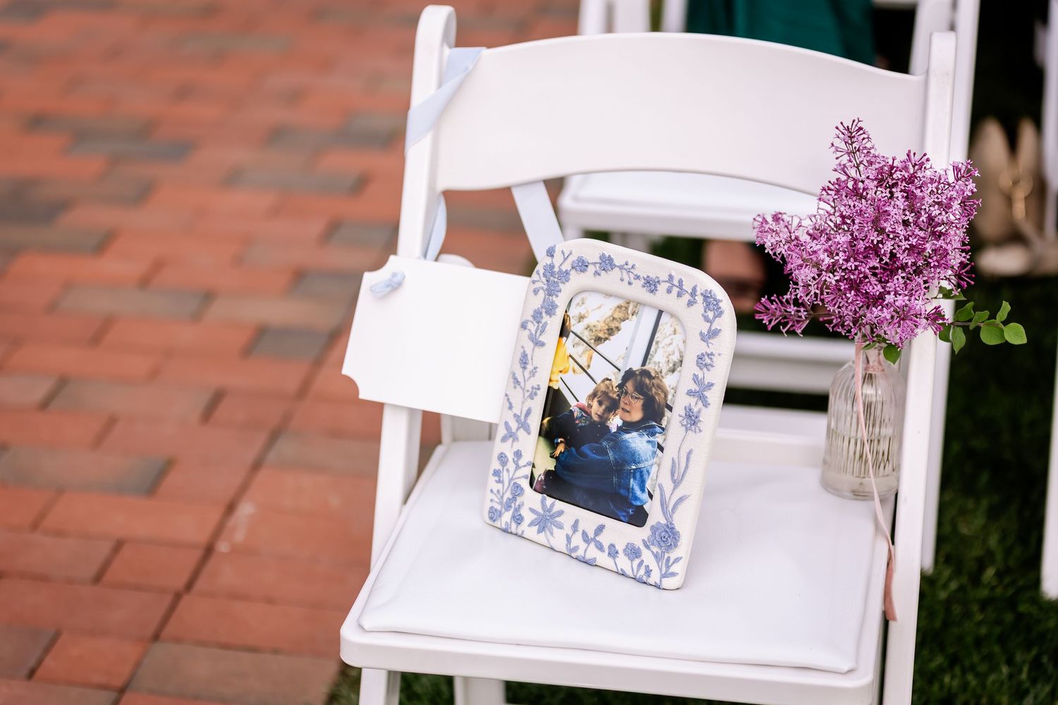 A white wedding ceremony chair decorated with lilac flowers and a framed photo.