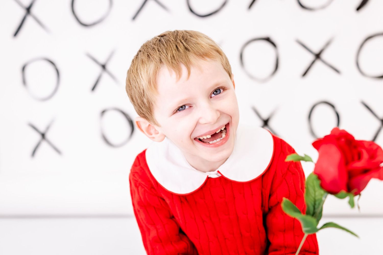 Young person in red top smiling against X's and O's backdrop with red roses.