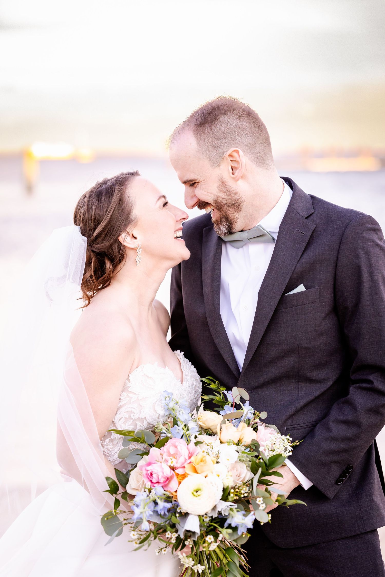 A joyful wedding couple shares a candid moment with a colorful bouquet featuring pink and white flowers.