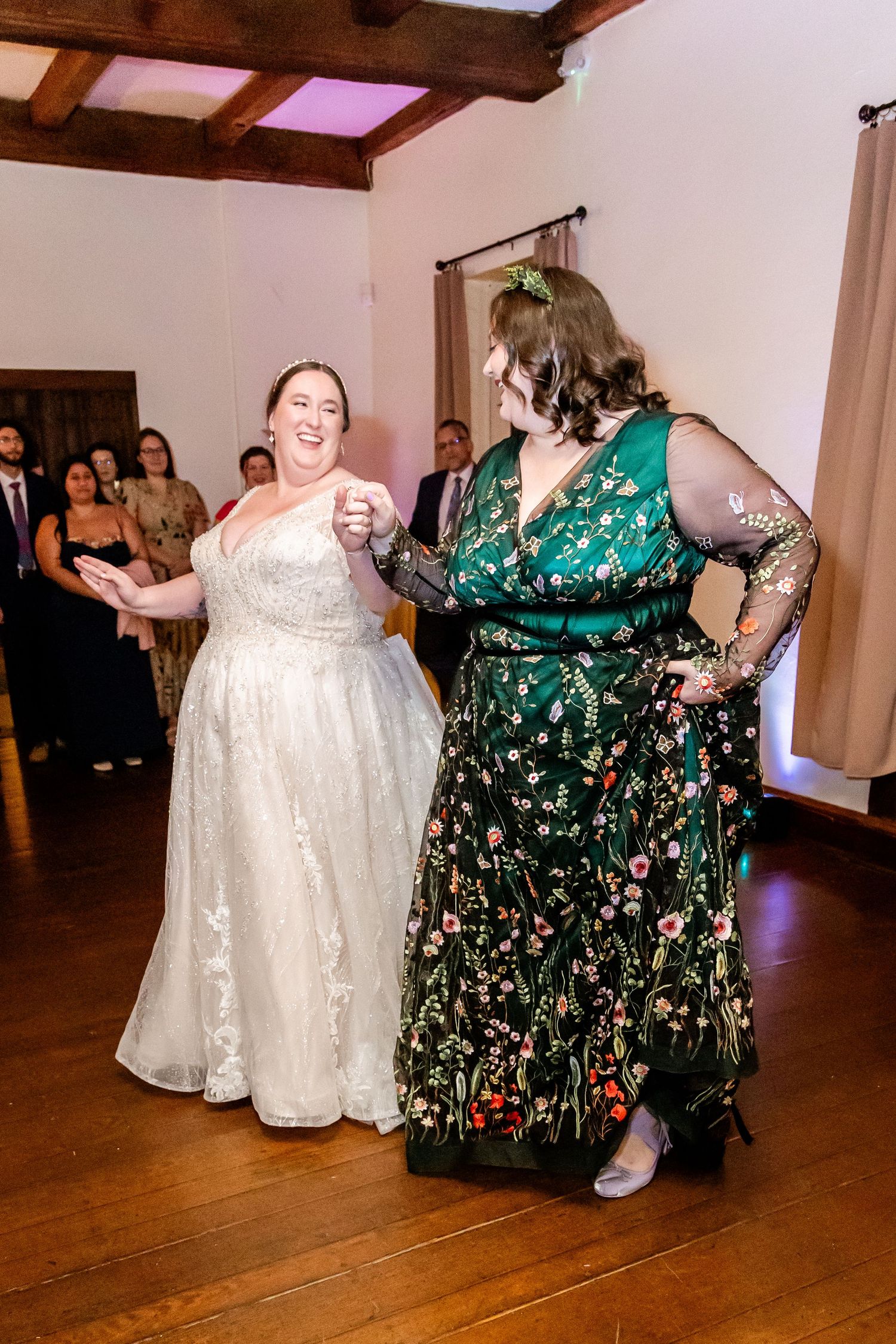Two wedding guests dancing together on wooden floor during reception celebration.