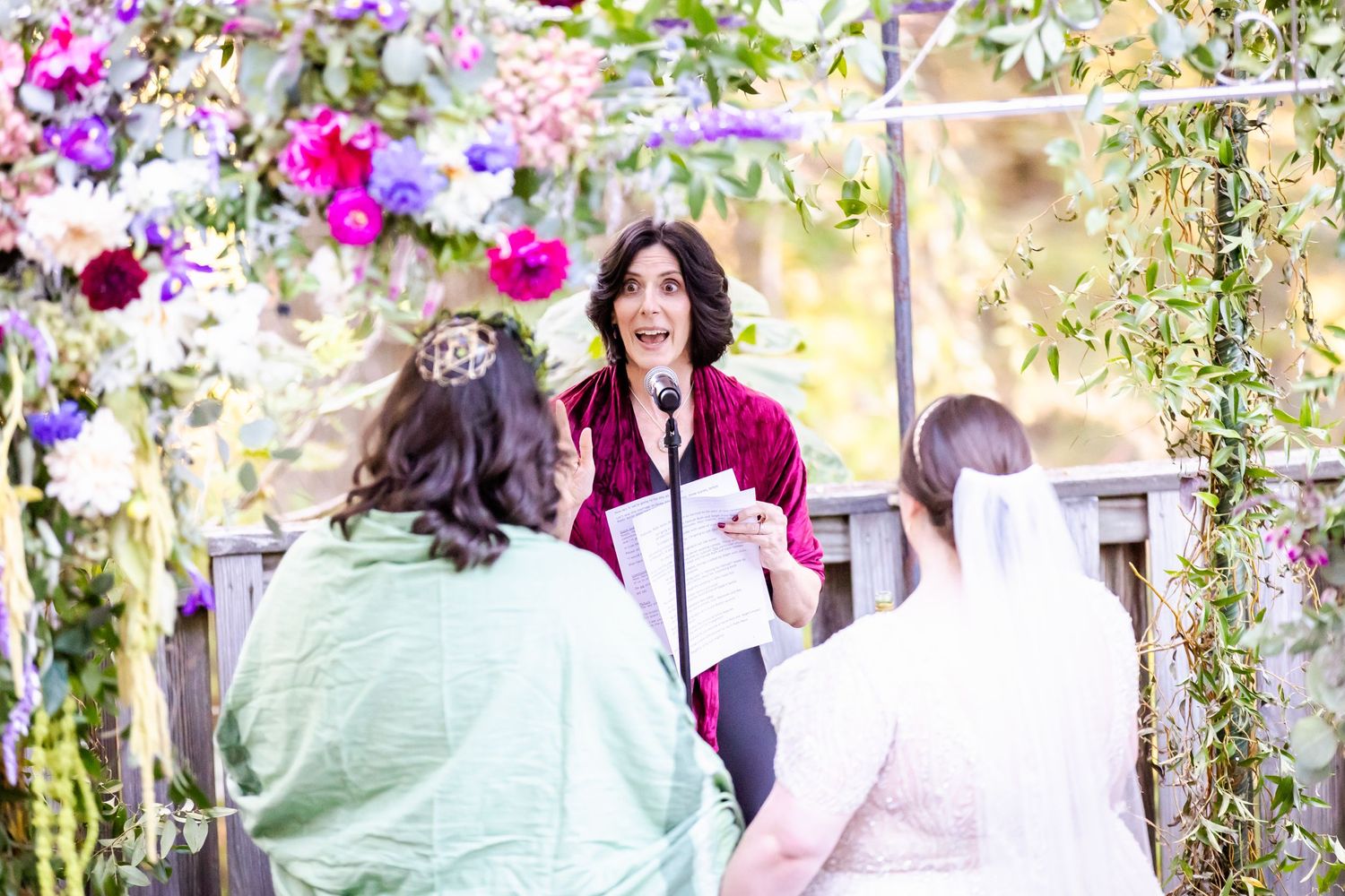 A wedding ceremony under a flower-covered arch with colorful blooms and greenery.
