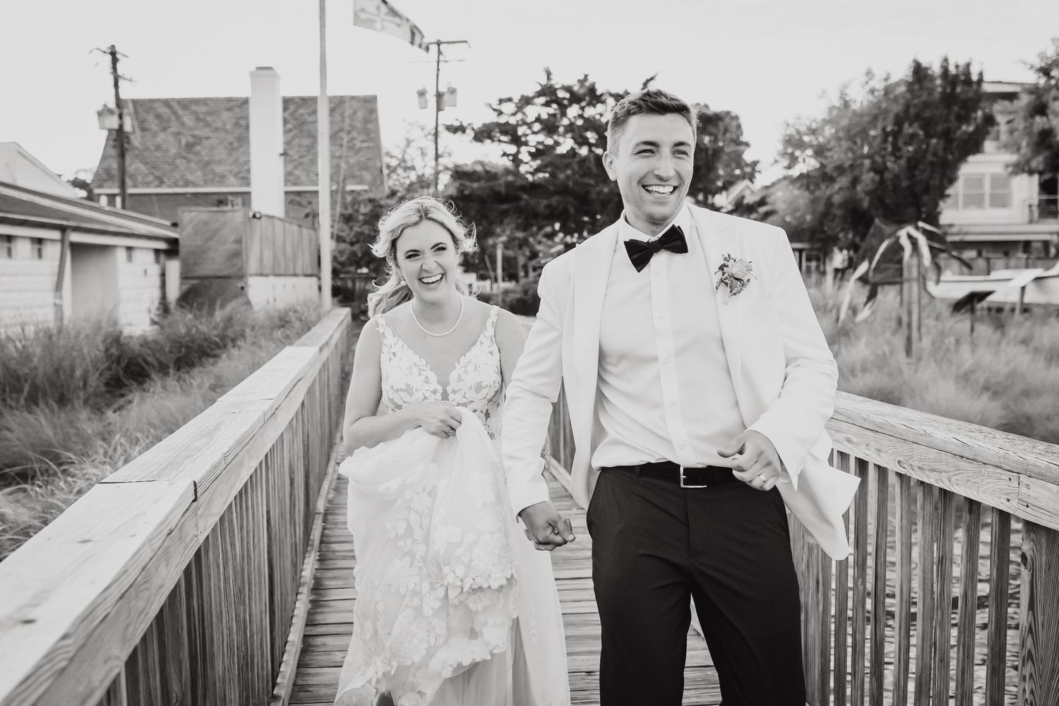 A happy couple walking on a wooden boardwalk, with the bride in a flowing lace dress.