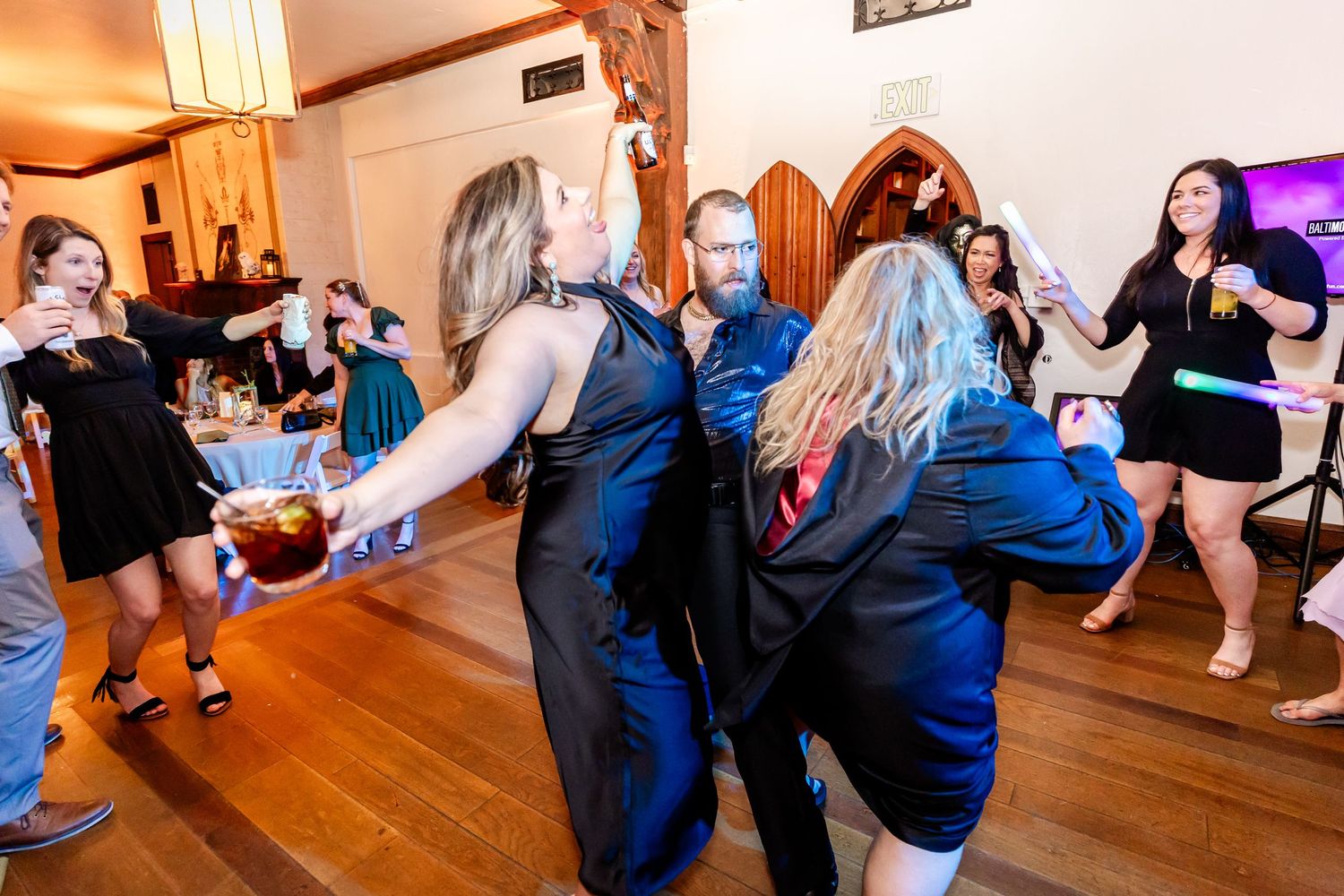 Group of party guests dancing on wooden floors with gothic archways and warm lighting.
