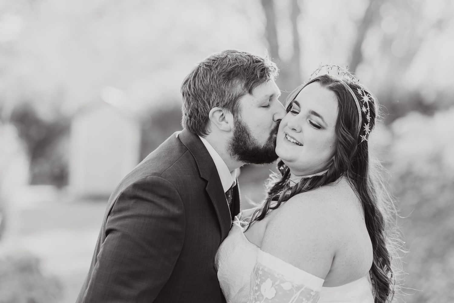 A romantic black and white wedding portrait of a couple sharing an intimate moment outdoors.