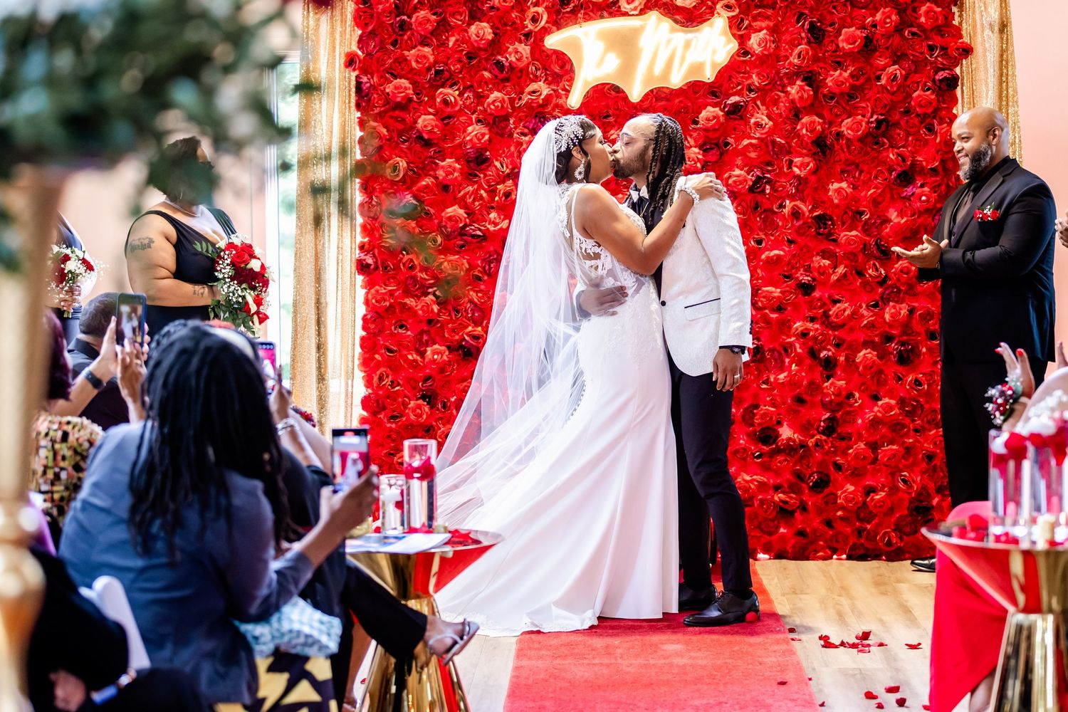 Wedding ceremony in front of stunning red rose wall backdrop with guests watching.