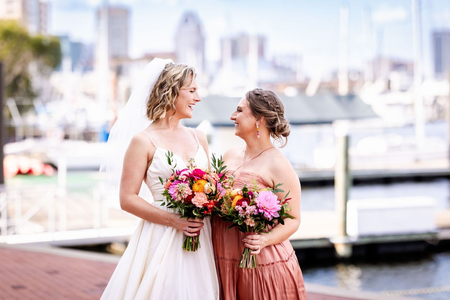Two people sharing joyful moment with colorful bouquets against harbor backdrop.