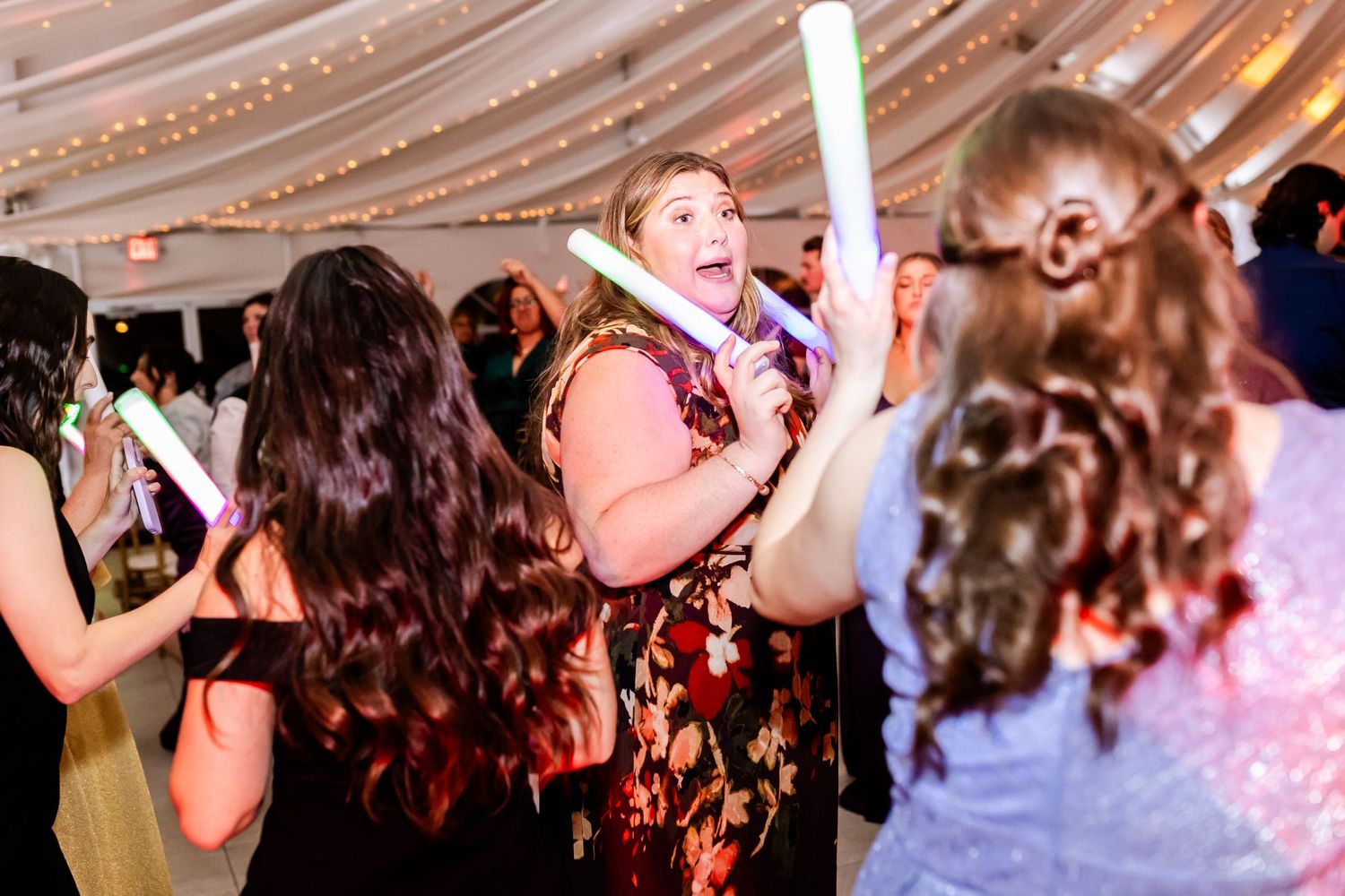 Wedding guests dance enthusiastically under decorative tent lighting at reception celebration.