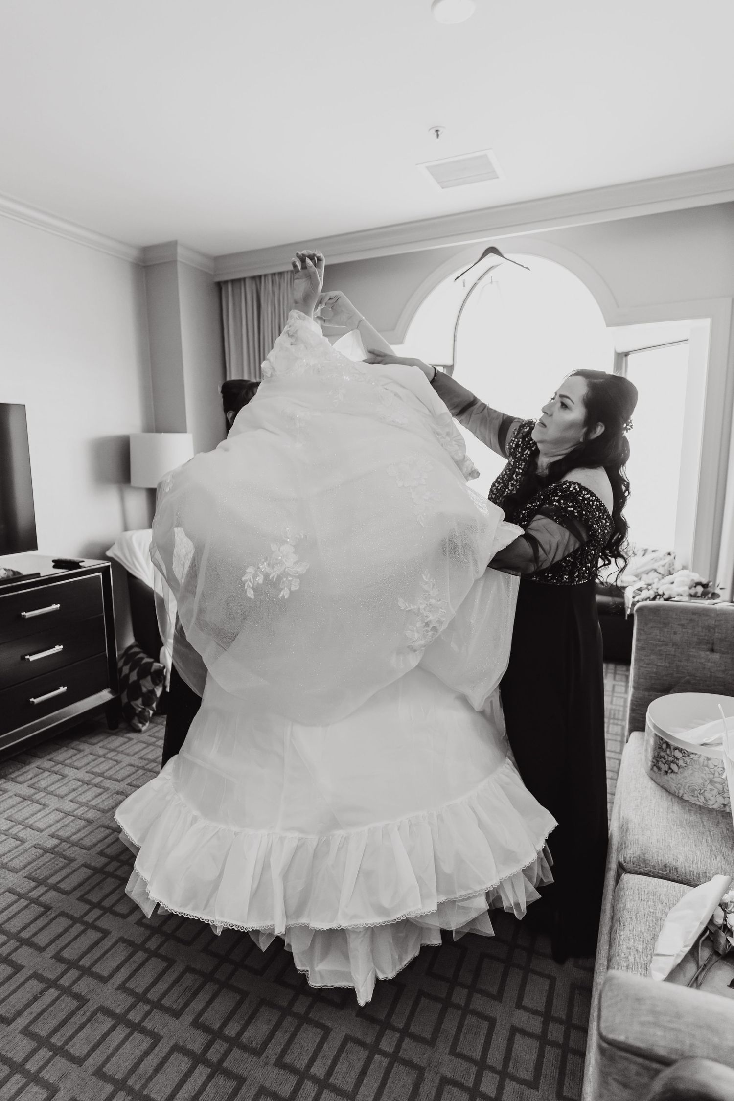 Black and white photo of a wedding dress being prepared in a hotel room.