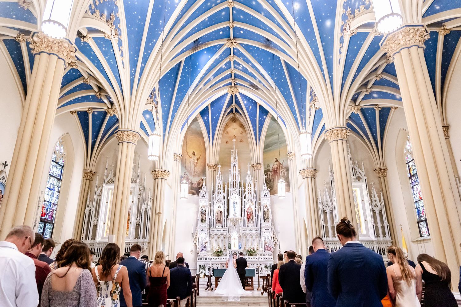Stunning cathedral interior with ornate Gothic vaulted ceilings and religious artwork during a wedding ceremony.