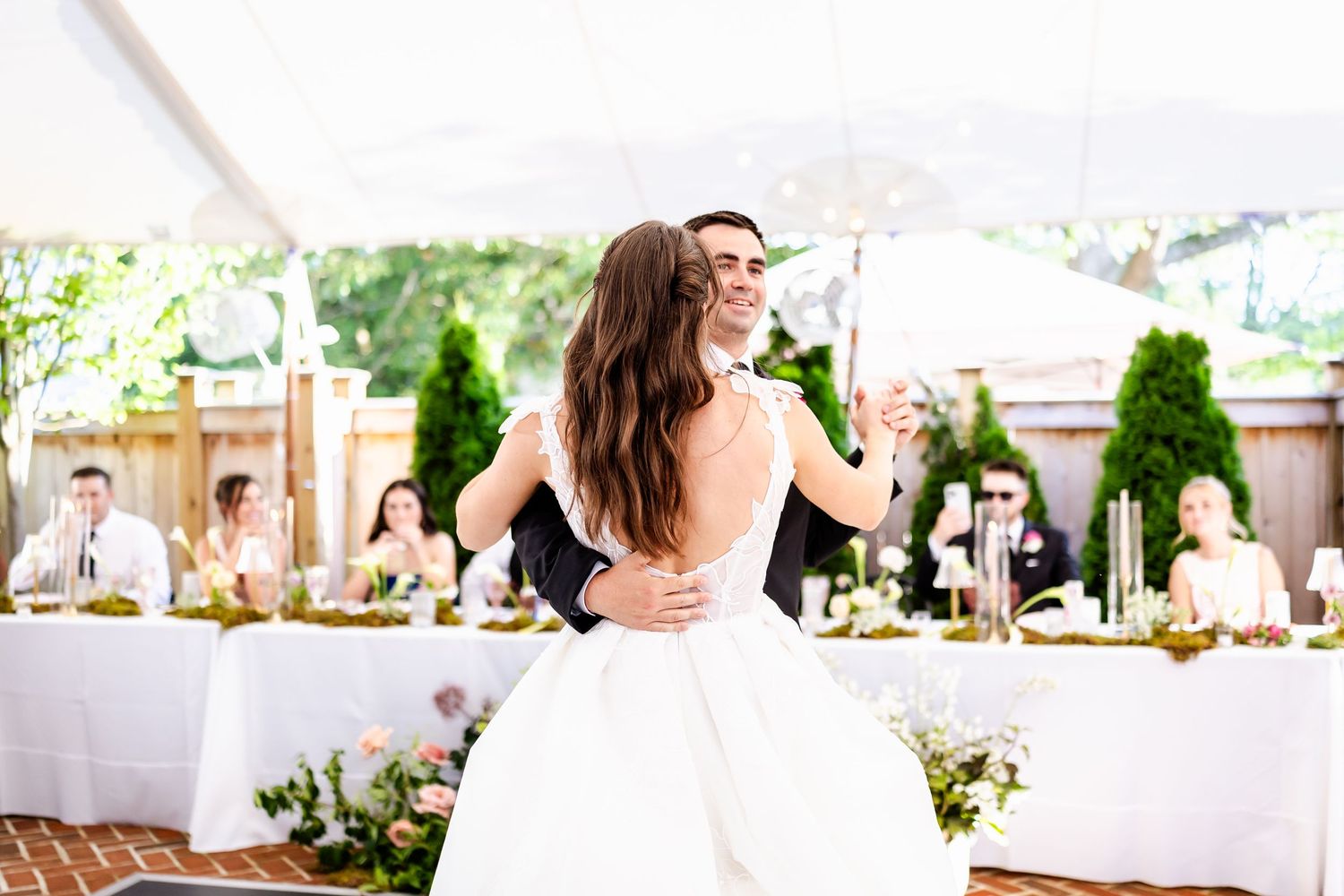 A beautiful outdoor wedding reception setup with white tables, floral arrangements and elegant decor under a tent.