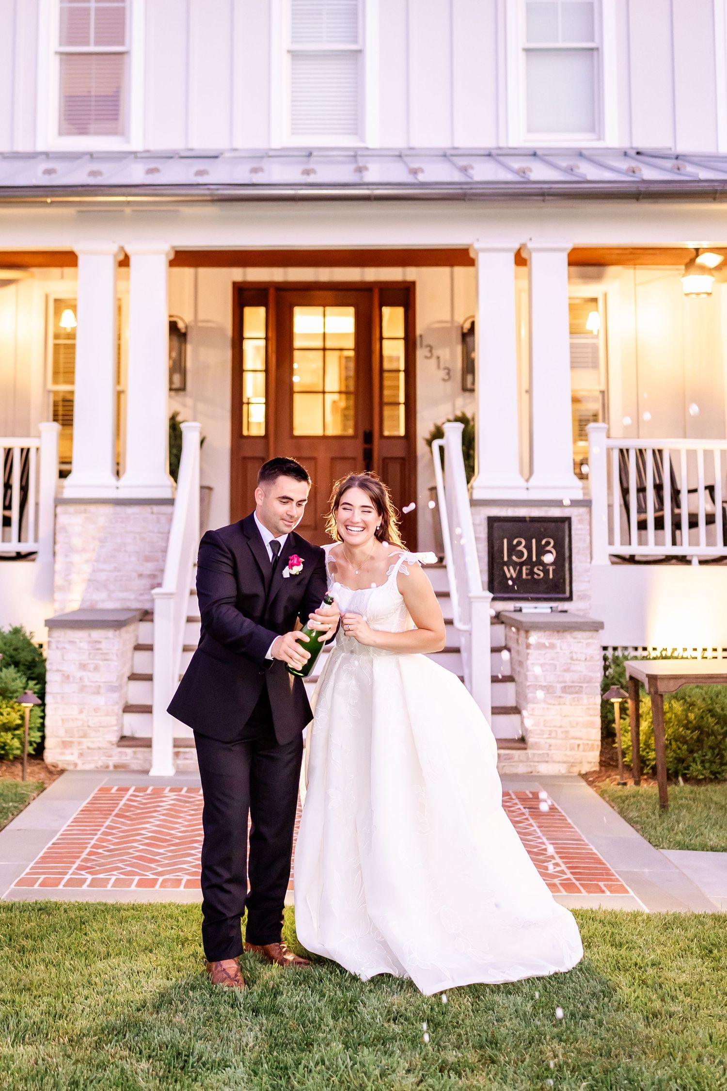 Newlyweds celebrate with champagne on the lawn in front of a white building with columns.