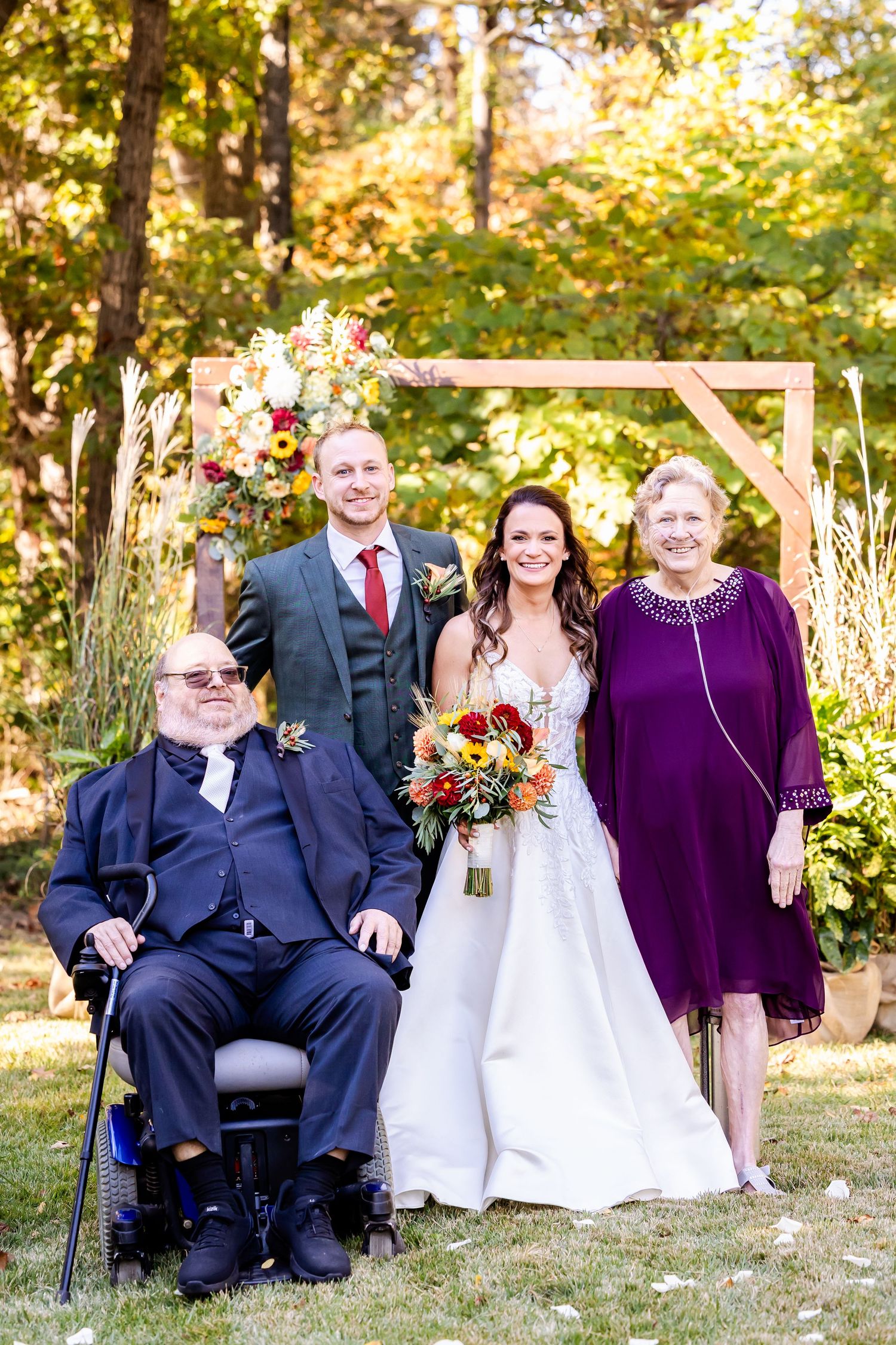 Wedding party poses outdoors in formal attire against autumn foliage backdrop.
