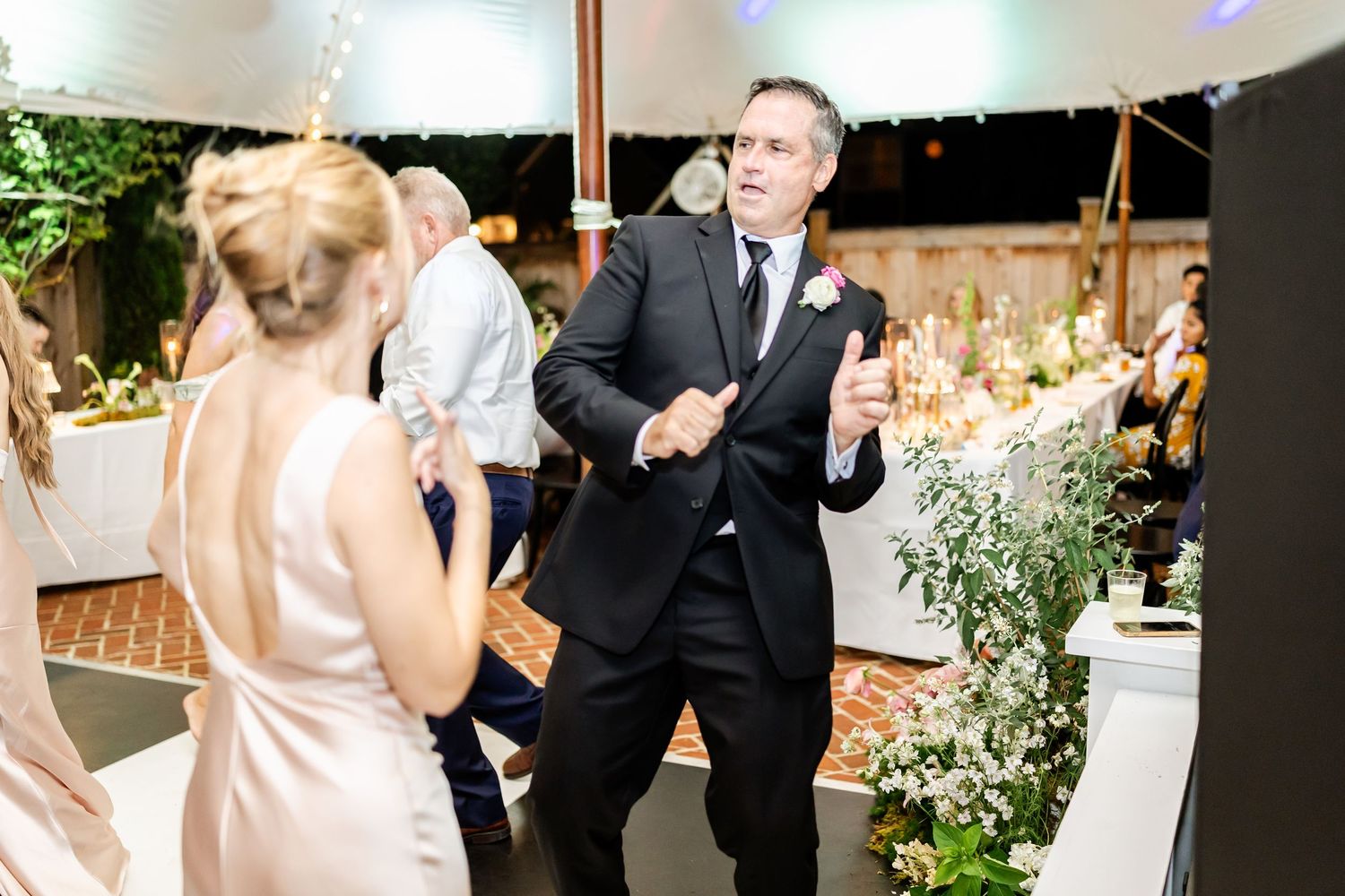 Guests dancing and celebrating at an elegant wedding reception under a white tent with floral decorations.