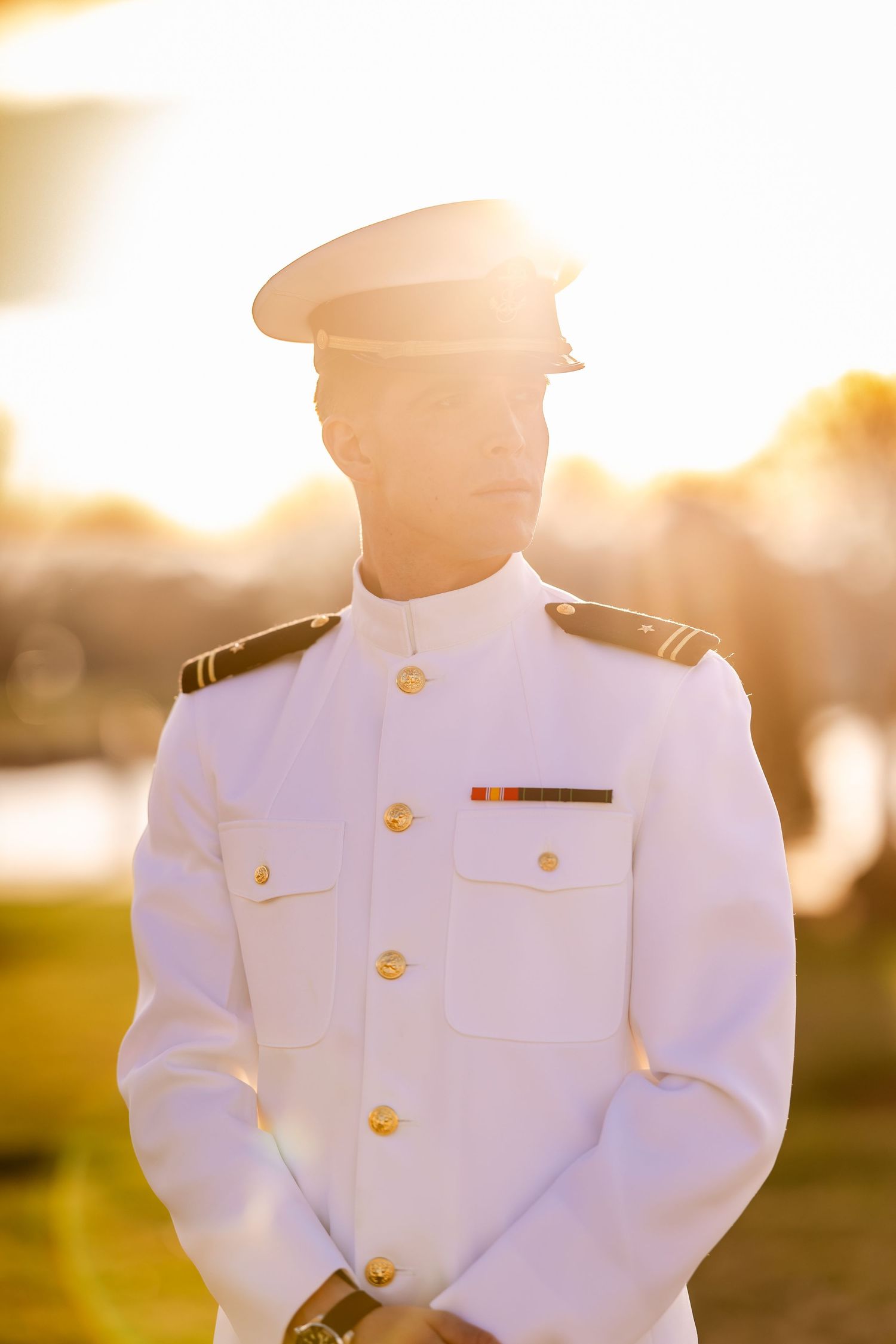 Naval officer in white dress uniform stands at attention during golden hour sunset.