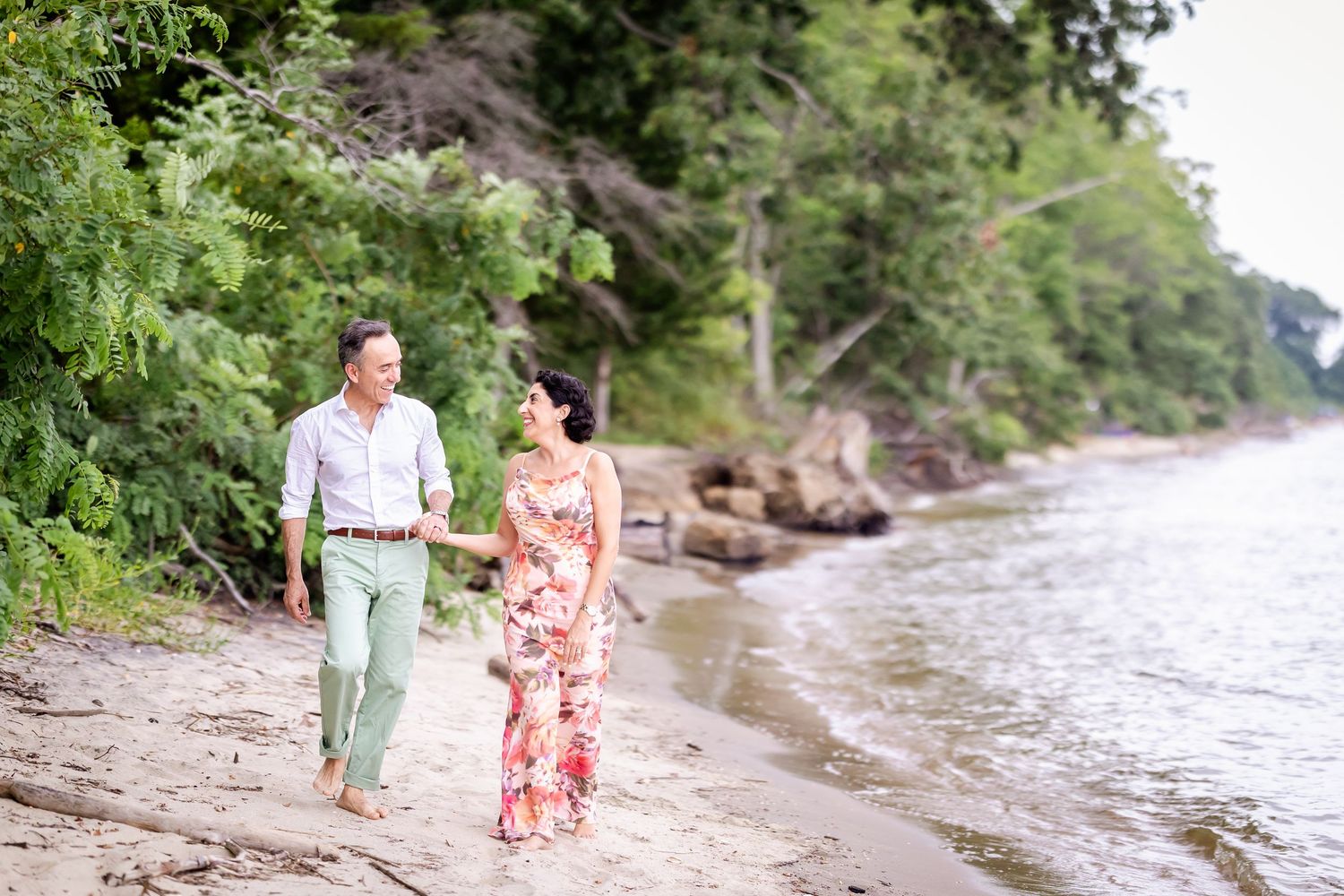 Two people walk hand in hand along a rocky riverbank on a sunny summer afternoon.