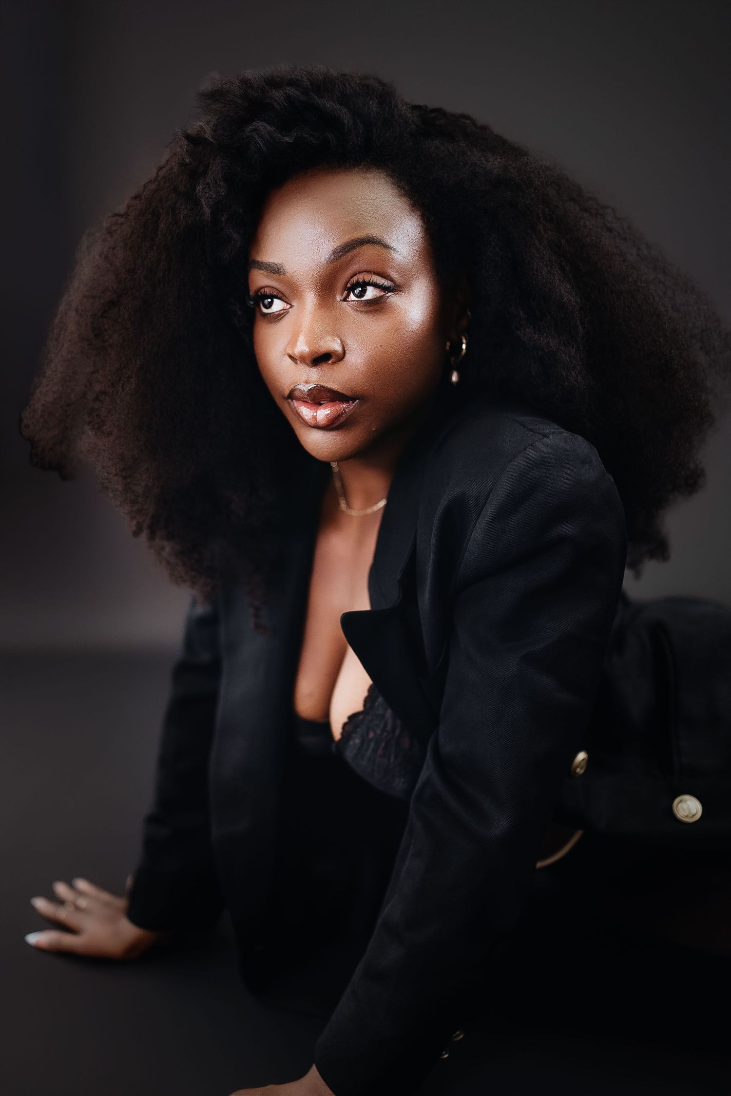 Professional portrait of a person with voluminous natural hair wearing a black blazer against a dark background.