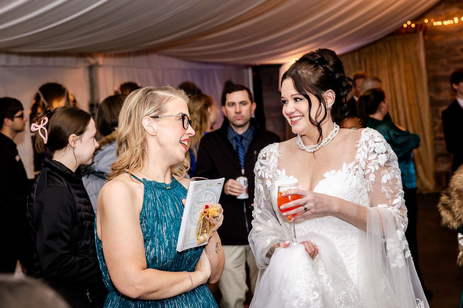 Wedding reception guests enjoying drinks and conversation in an elegantly draped venue.