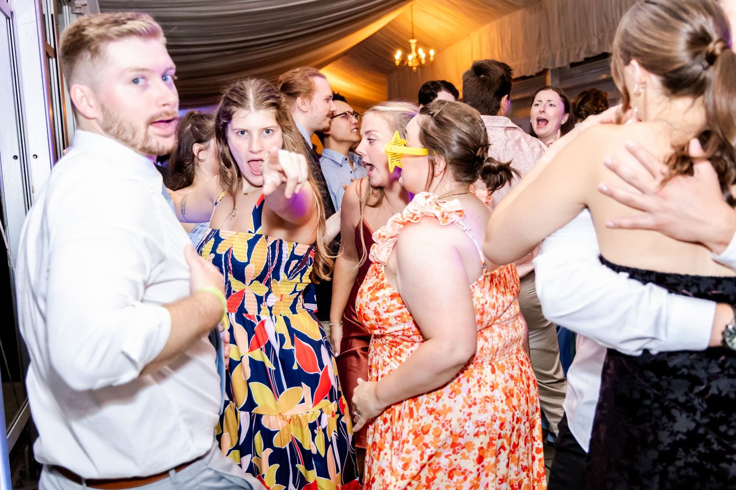 Wedding guests dancing and celebrating with joyful expressions during evening reception.