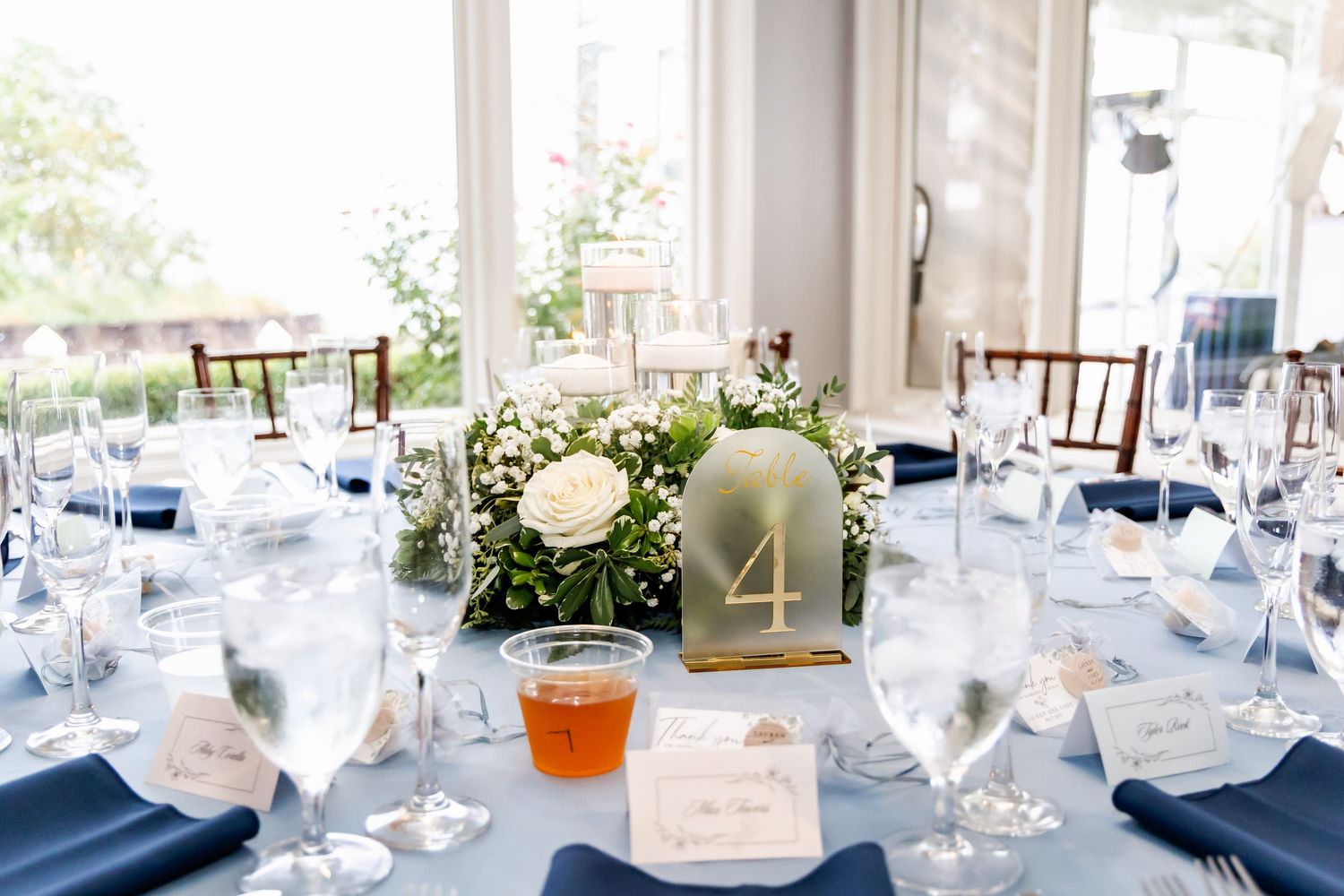 Elegant wedding reception table setup with white linens and glassware in bright sunlit venue.
