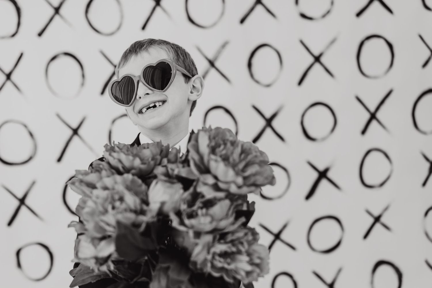 Stylish figure in black with heart-shaped sunglasses poses against a pattern of X's and O's in black and white.