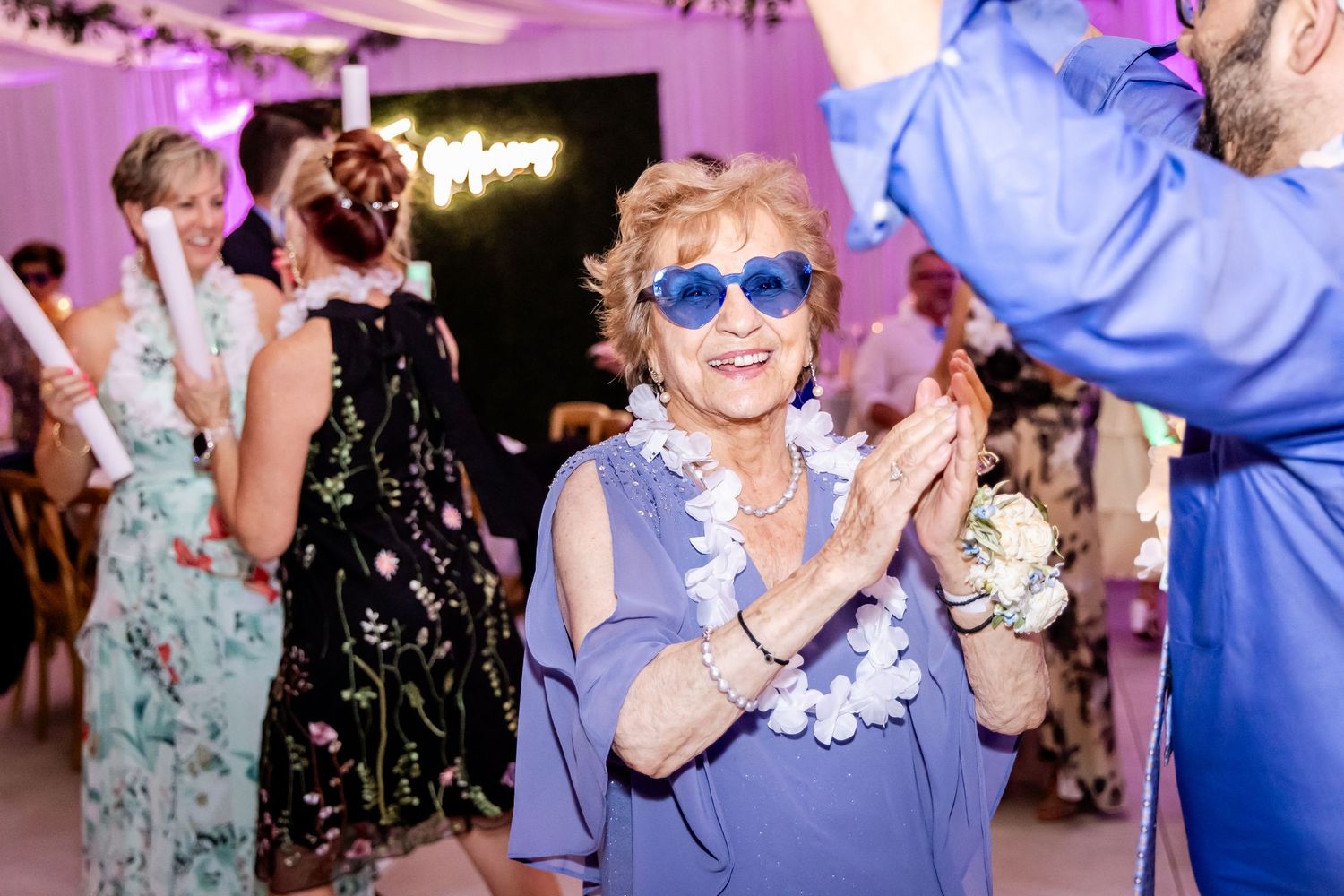 Wedding guests dancing under purple lighting at evening reception celebration.